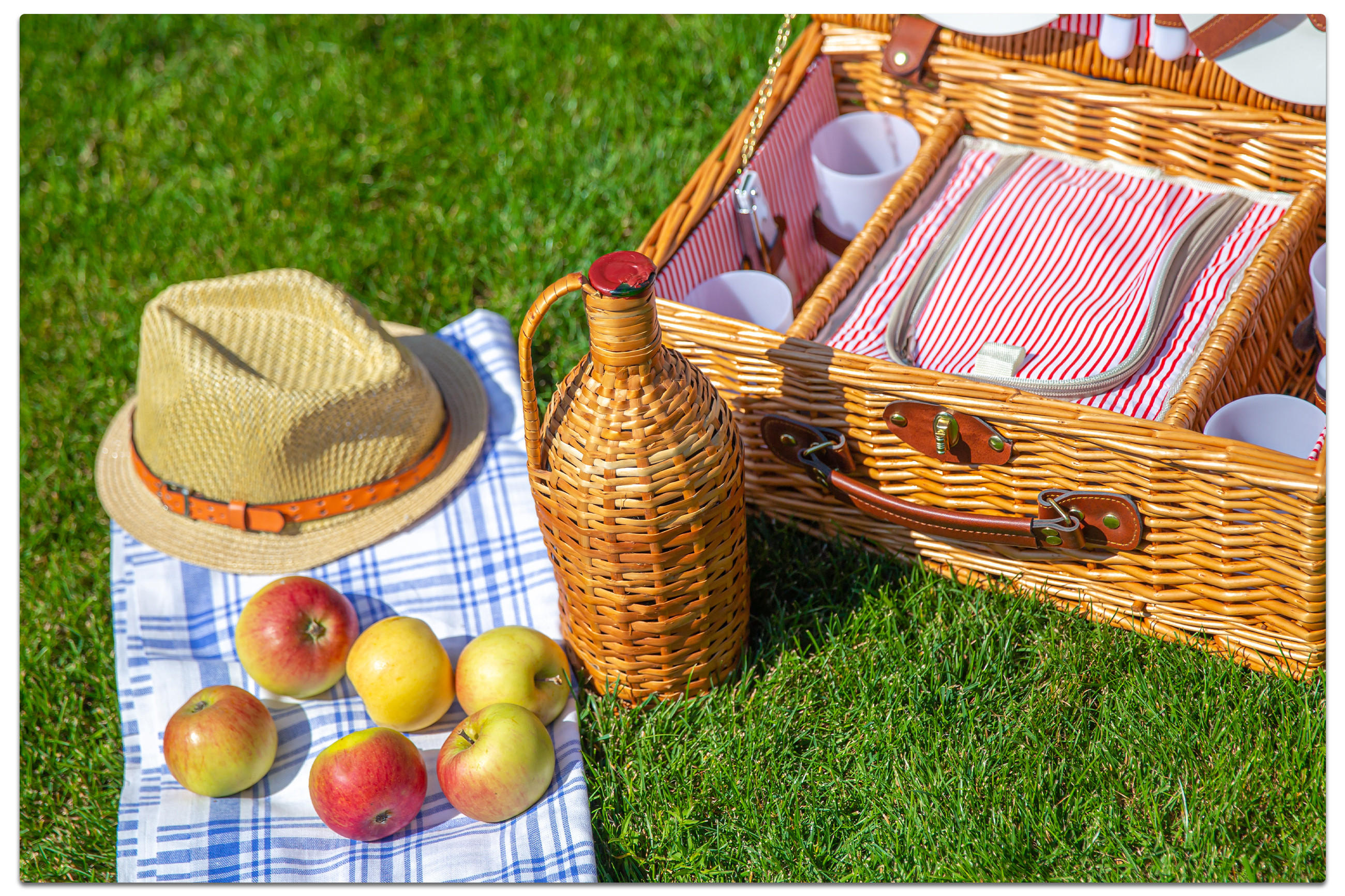 Ein Picknickkorb mit Äpfeln, einer Flasche Wein und einem Hut