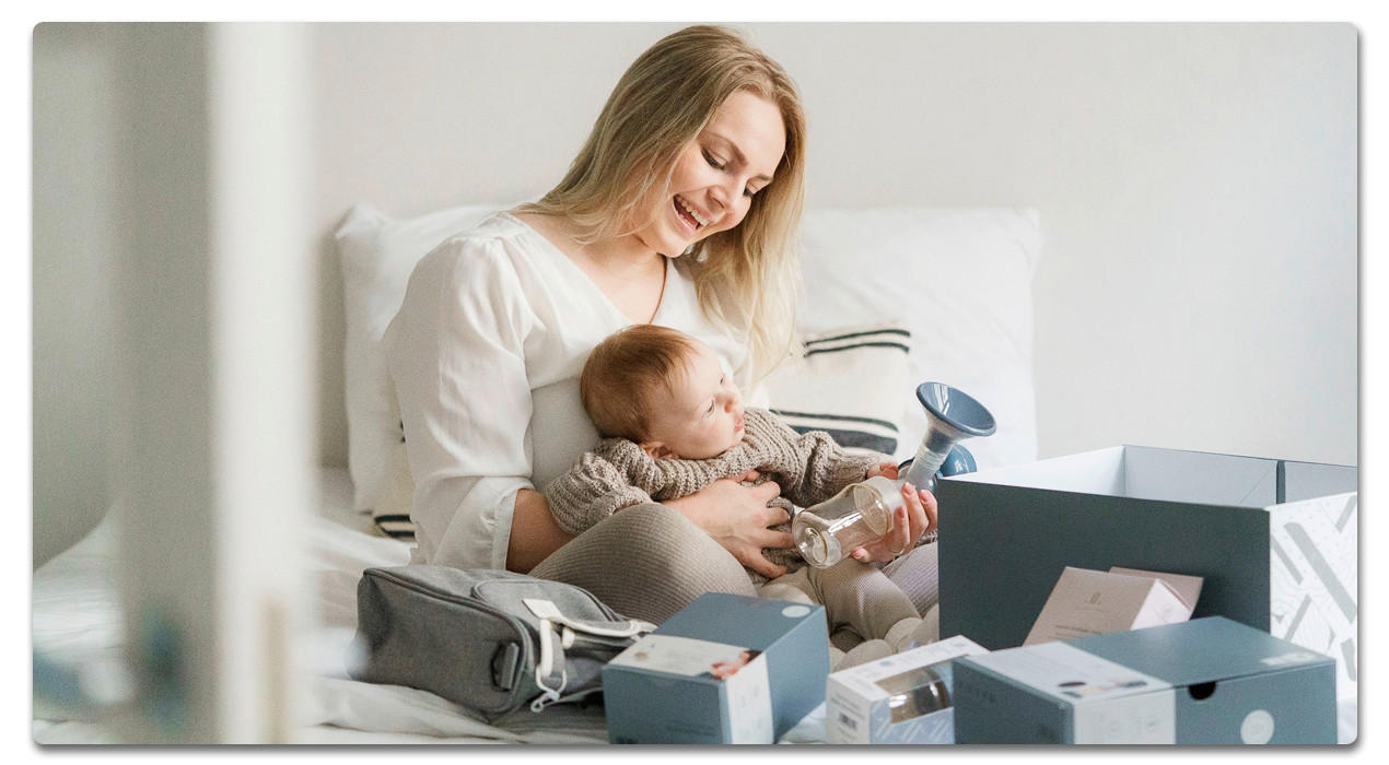 frau mit baby auf dem Schoß und Abpumpflasche auf dem bett