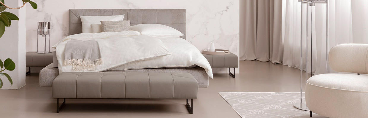 graues Bett mit heller bettwäsche und hellen kissen