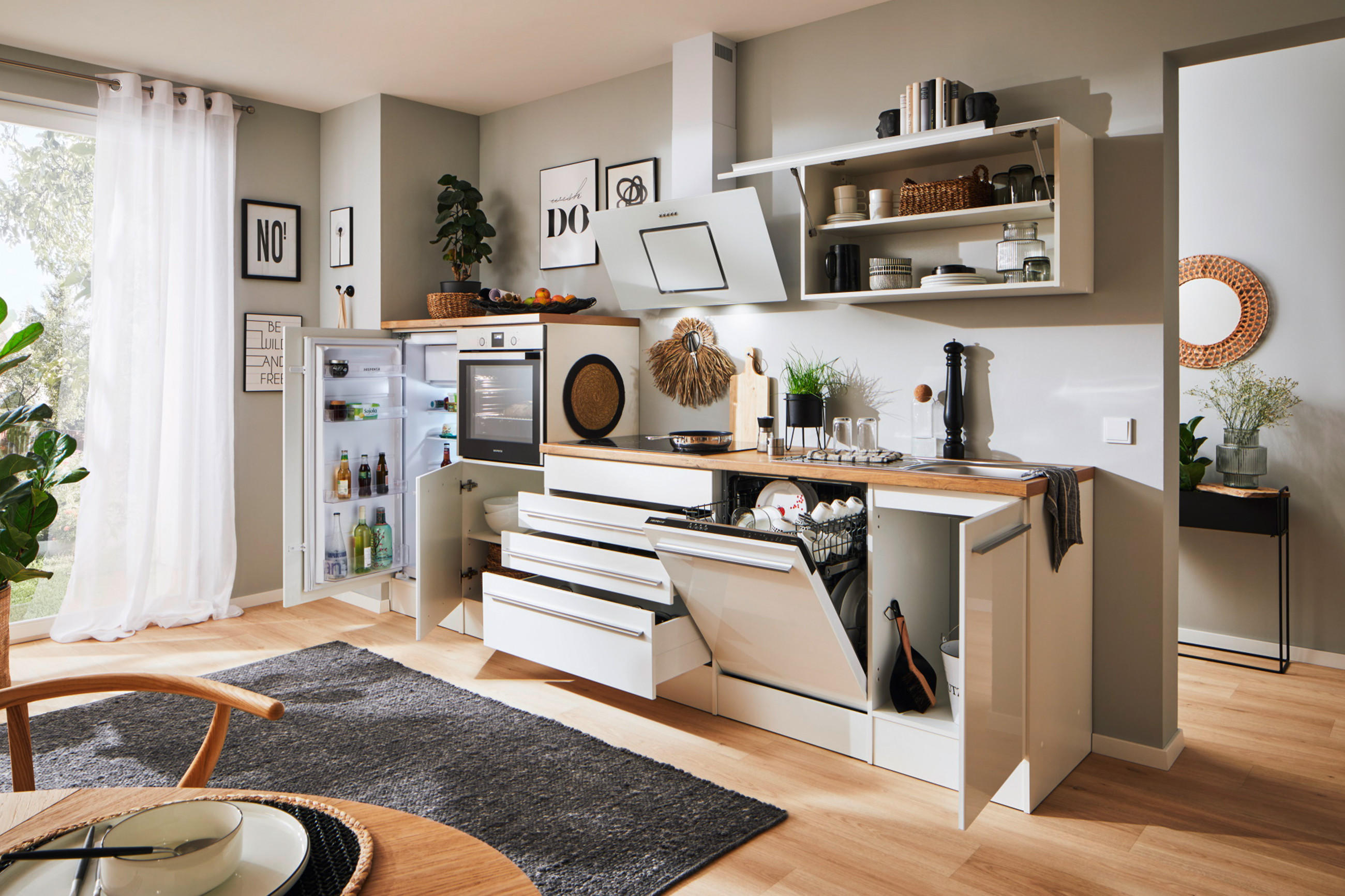 Weiße Komplettküche mit offenen Schubladen und Türen, mit Elektrogeräten und Kochutensilien.