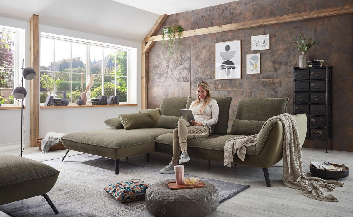 Moderano ECKSOFA Olivgrün Flachgewebe, links davon: Hochflorteppich, Kissen, rechts davon: Highboard, Lektüre in hellem Wohnzimmer.