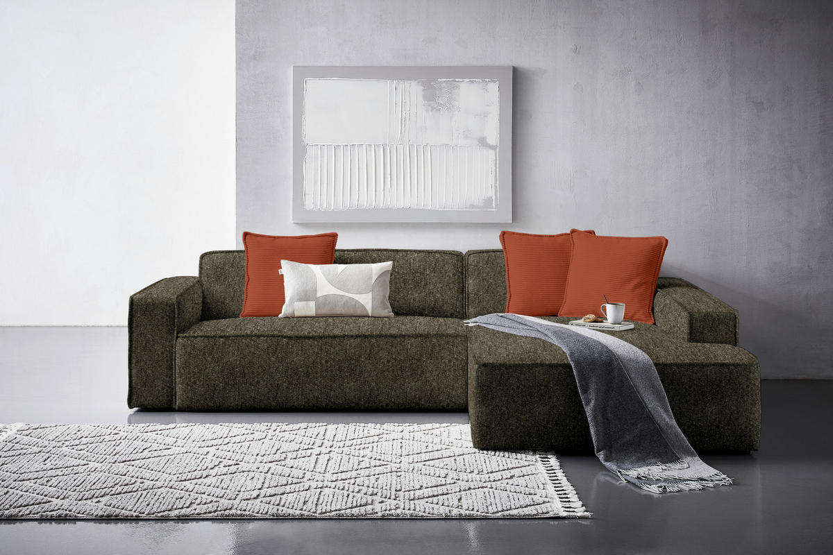 Carryhome ECKSOFA Olivgrün Chenille, links davon: Hochflorteppich in weiß, rechts davon: Decke, Bild in weiß in hellem Wohnzimmer.