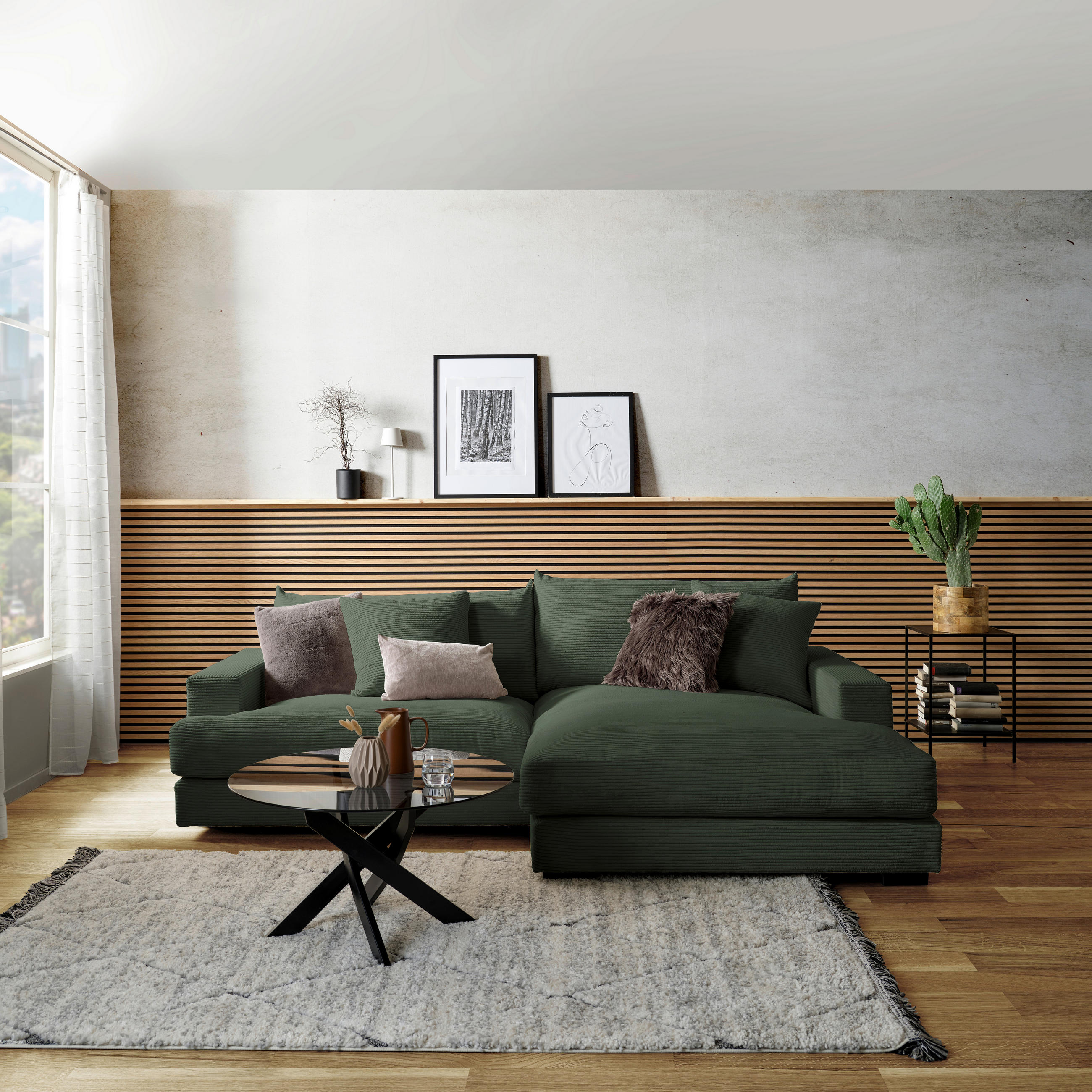 P & B ECKSOFA Dunkelgrün Cord, links davon: Hochflorteppich, rechts davon: Kissen, Bild in weiß, Topfpflanze in grün in hellem Wohnzimmer.