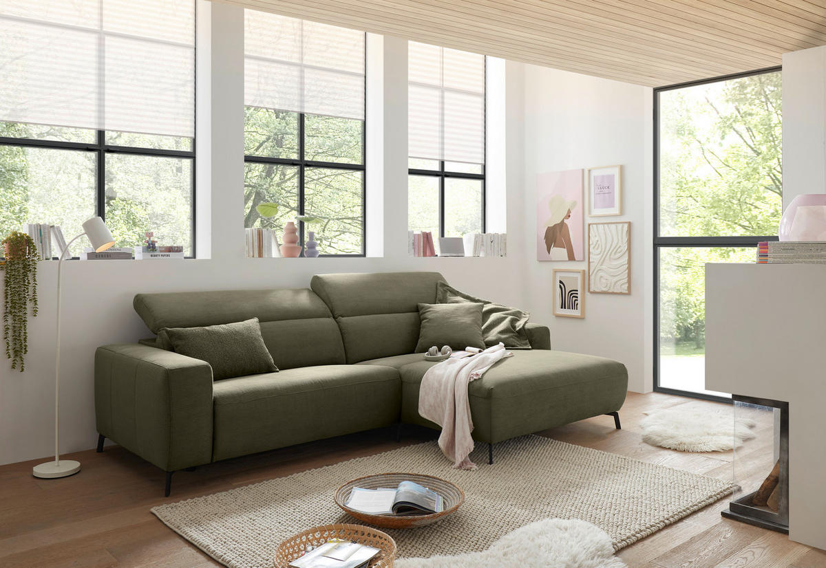 Pure Home Lifestyle ECKSOFA Olivgrün Feincord, rechts davon: Hochflorteppich, Schale, Decke in grün, Jalousie in weiß in hellem Wohnzimmer.