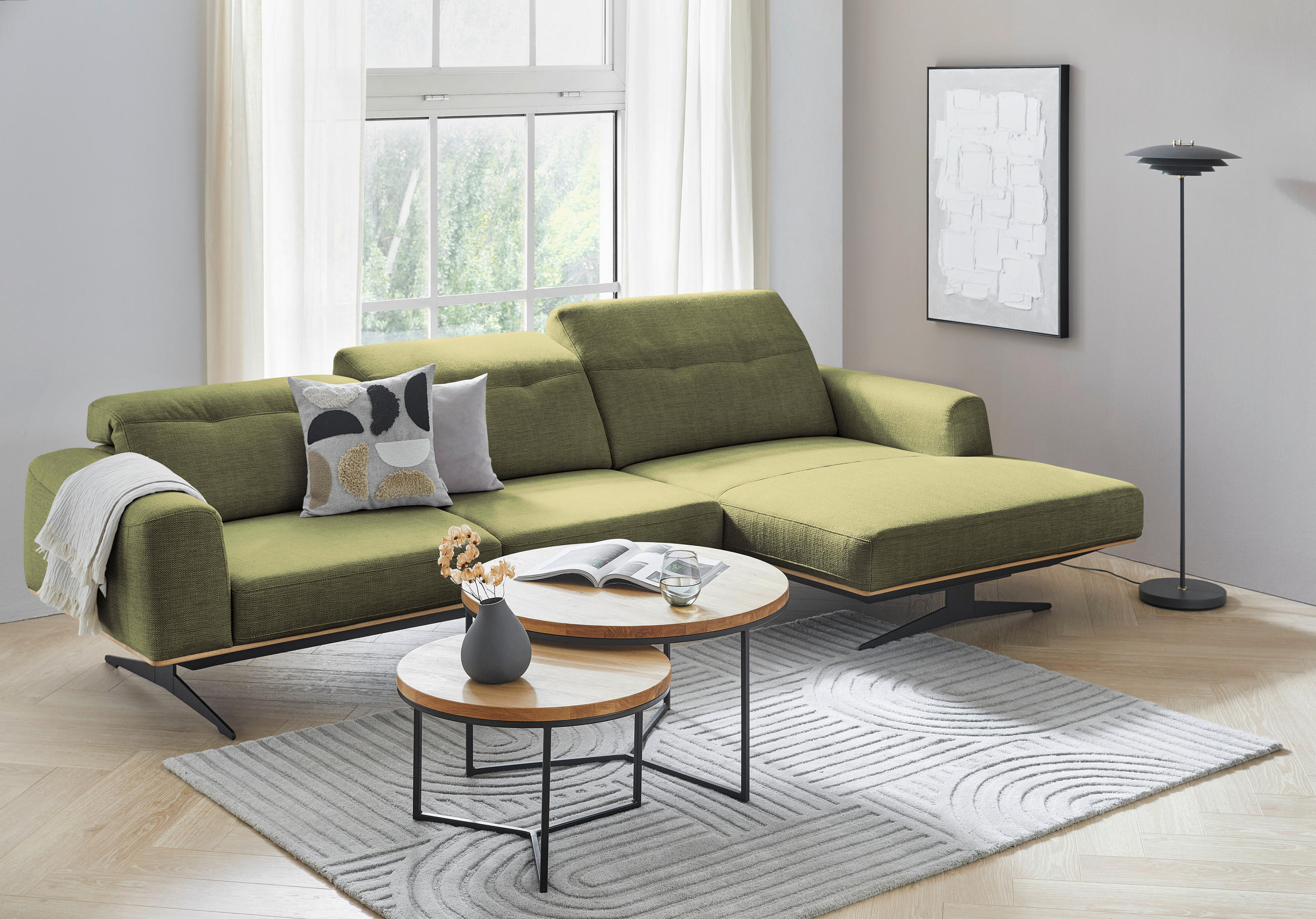 Novel ECKSOFA Olivgrün Struktur, links davon: Kissen, rechts davon: Webteppich, Couchtisch, Lektüre in weiß in hellem Wohnzimmer.