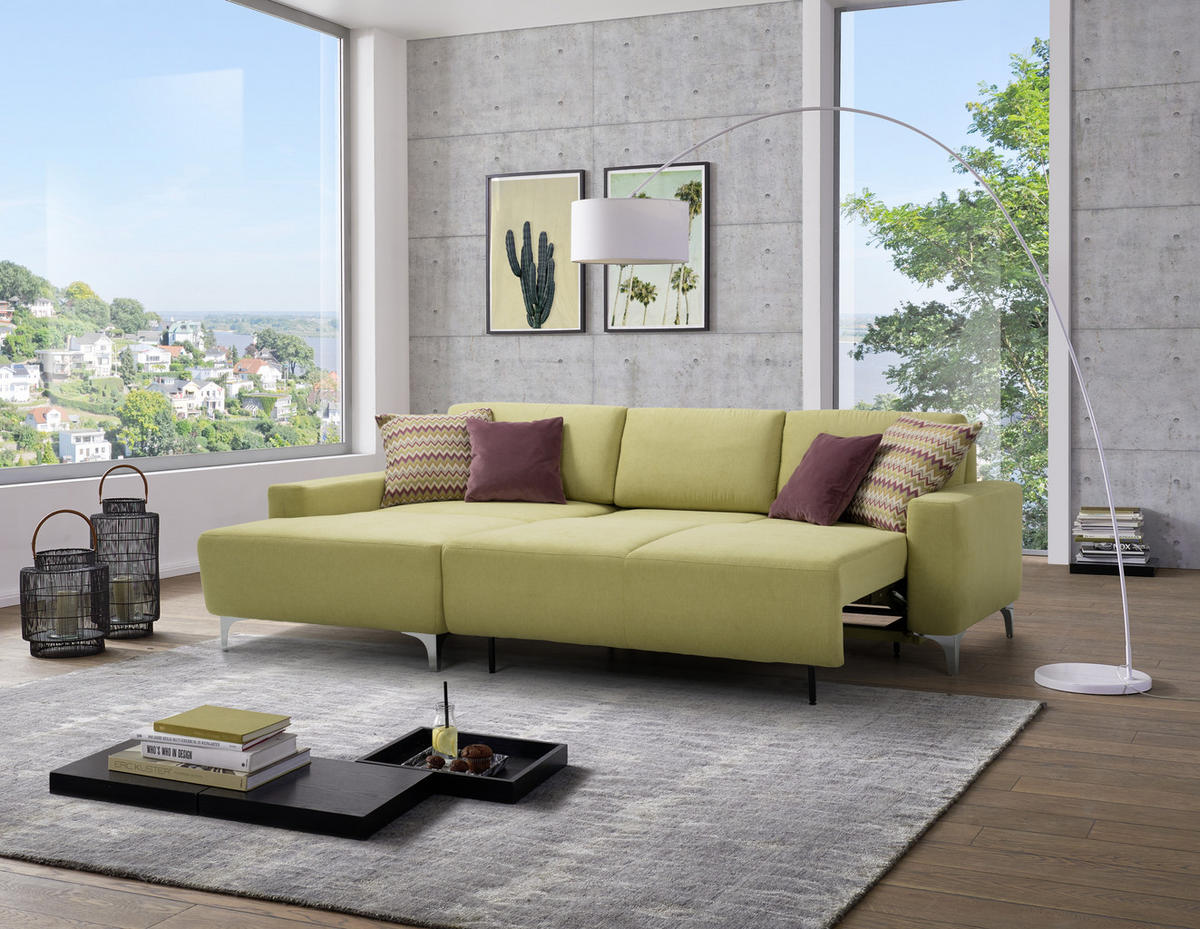 Sedda ECKSOFA Hellgrün Chenille, links davon: Hochflorteppich, Lektüre, rechts davon: Kissen in lila, Bild in grün in hellem Wohnzimmer.
