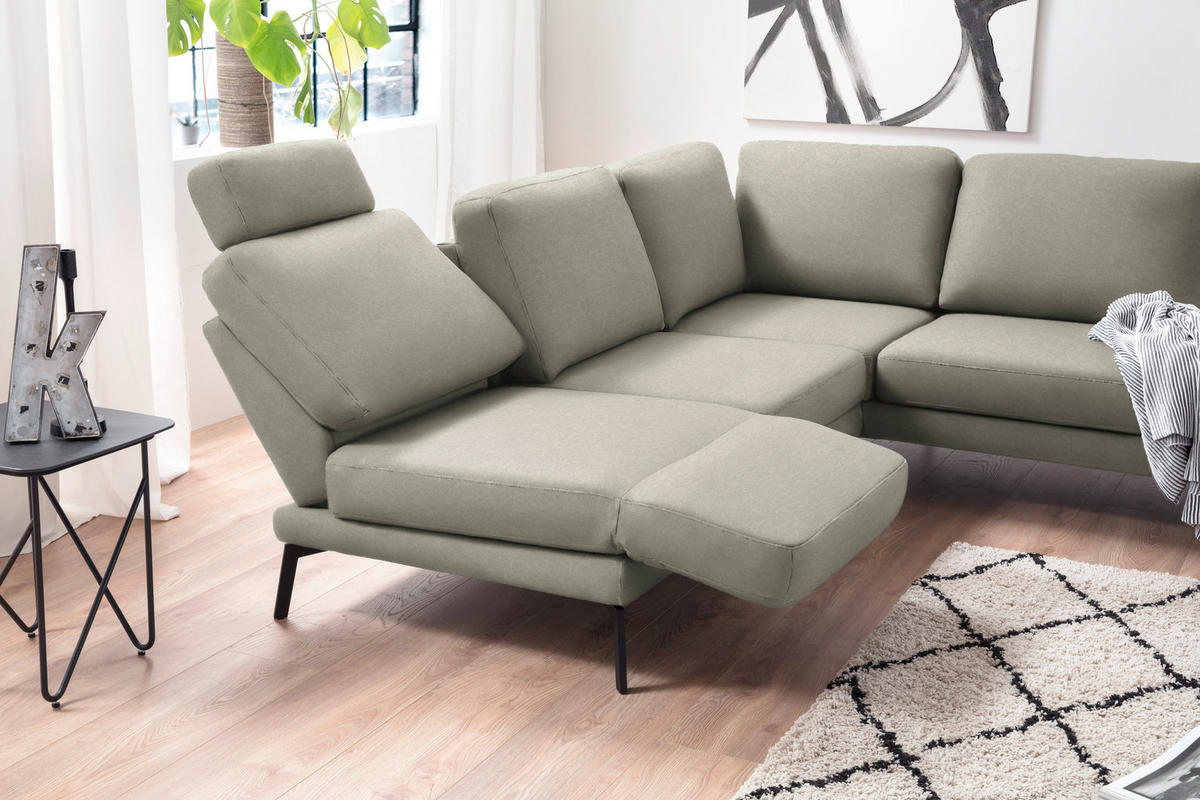 Hom`in ECKSOFA Olivgrün Mikrofaser, links davon: Beistelltisch in schwarz, Gardine, Store in grau, rechts davon: Hochflorteppich in weiß in hellem Wohnzimmer.