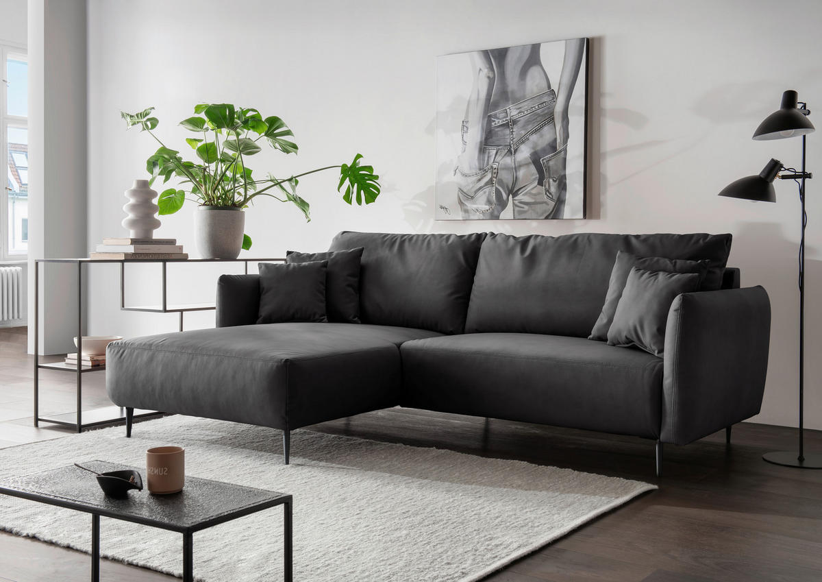 Livetastic ECKSOFA Schwarz Lederlook, links davon: Hochflorteppich, Couchtisch, Topfpflanze in grün, rechts davon: Bild in grau in hellem Wohnzimmer.
