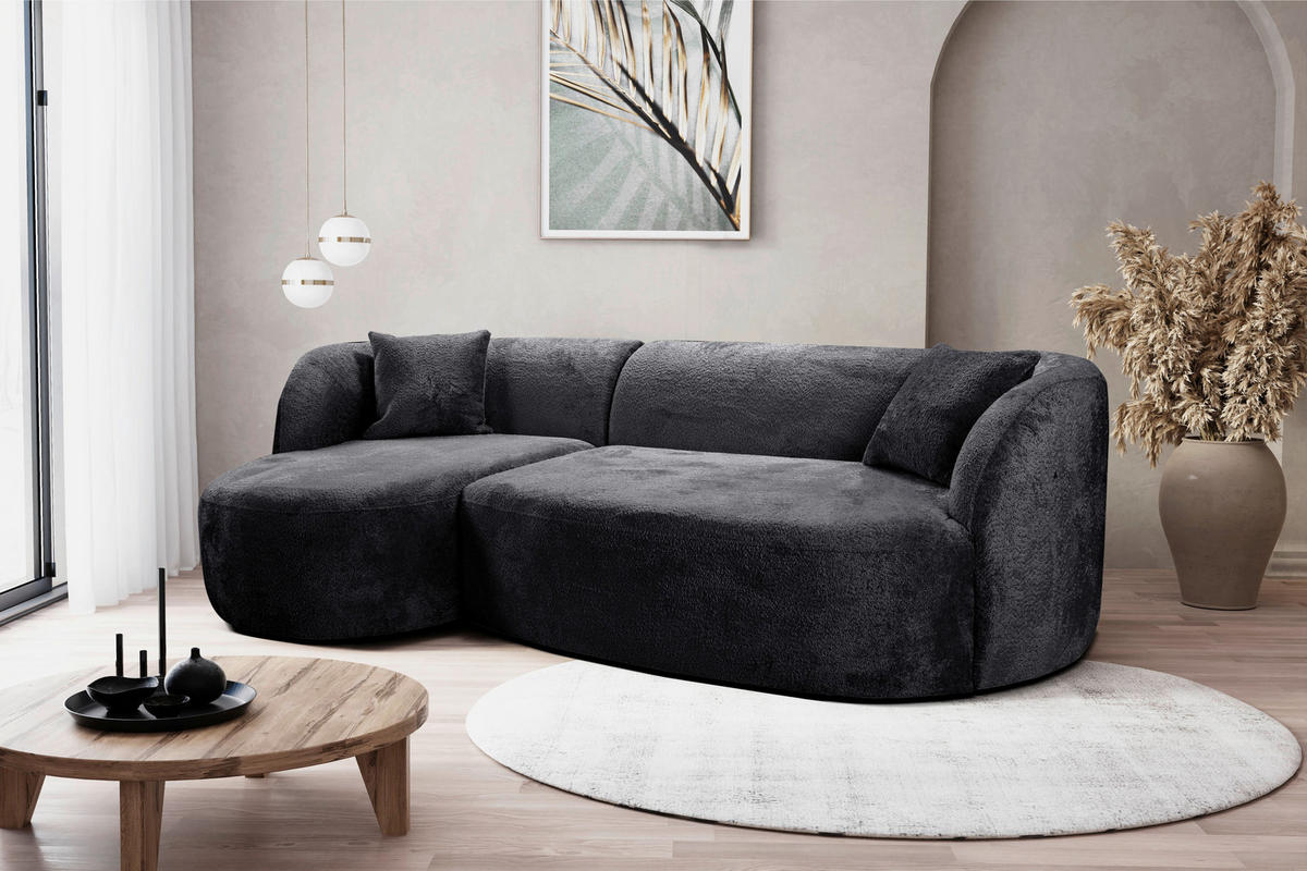 MID.YOU ECKSOFA Schwarz Bouclé, links davon: Beistelltisch in braun, rechts davon: Hochflorteppich in weiß, Topfpflanze, Blume in hellem Wohnzimmer.