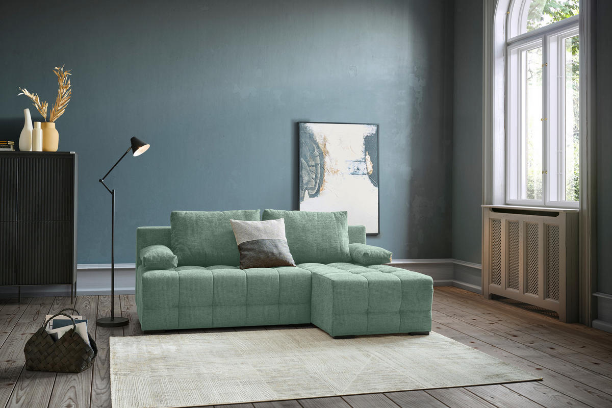 home24 ECKSOFA Dunkelgrün Chenille, links davon: Highboard, Stehleuchte in grün, rechts davon: Hochflorteppich, Bild in dunklem Wohnzimmer.