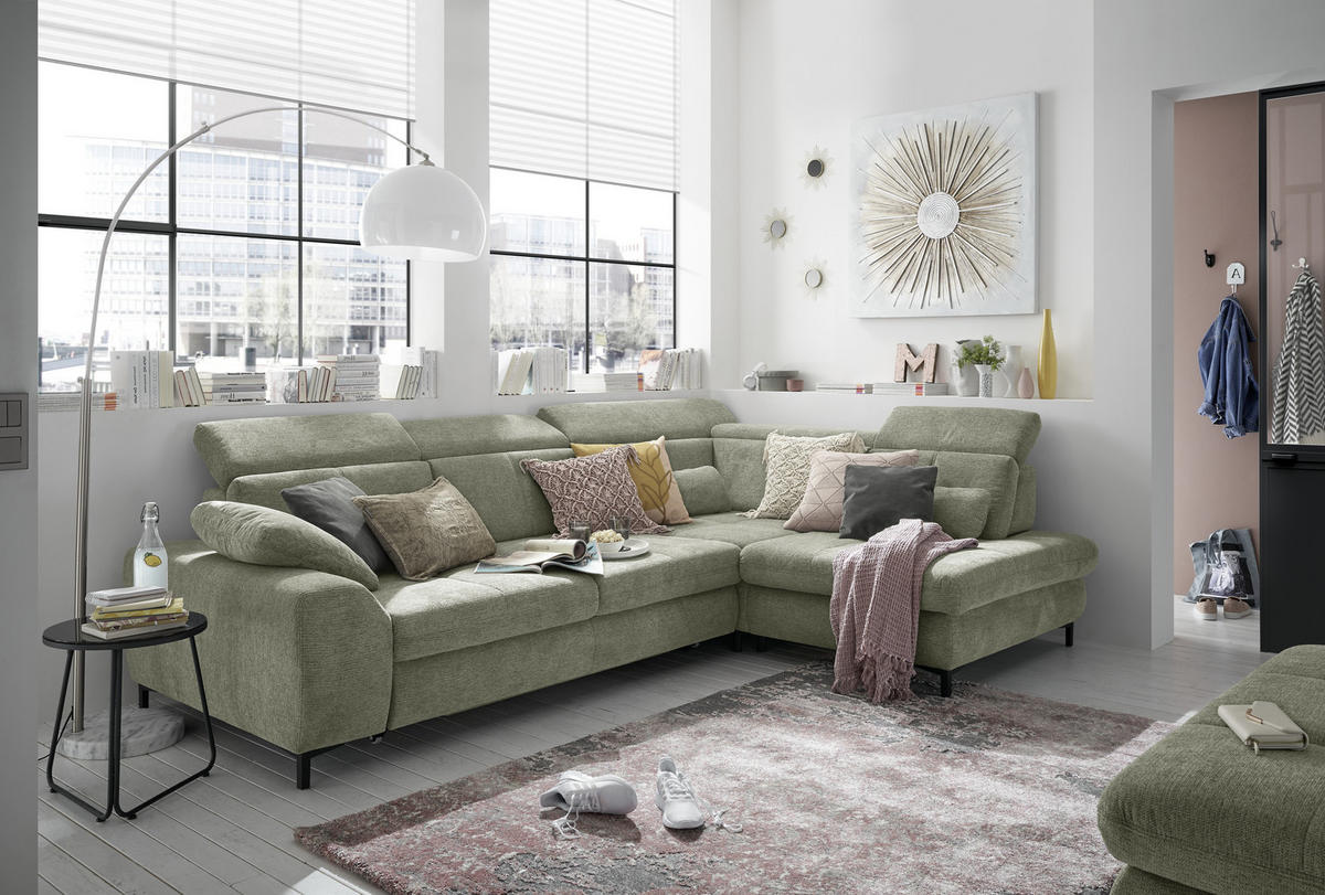 SetOne by Musterring ECKSOFA Grün Webstoff, links davon: Beistelltisch, rechts davon: Hochflorteppich, Hocker in grün, Jalousie in weiß in hellem Wohnzimmer.