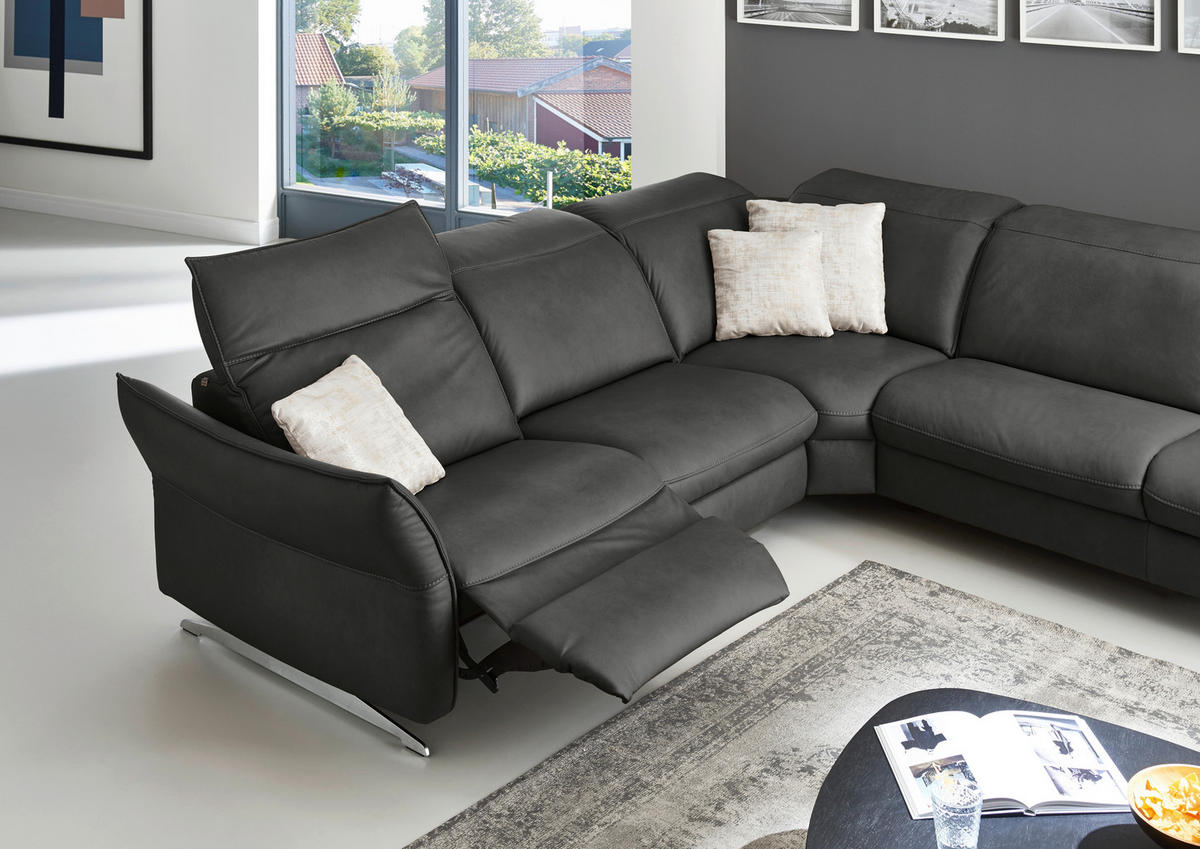 Hukla ECKSOFA inkl. Funktionen Valdera Schwarz Echtleder, links davon: Bild, rechts davon: Hochflorteppich, Lektüre in weiß, Kissen in weiß in dunklem Wohnzimmer.