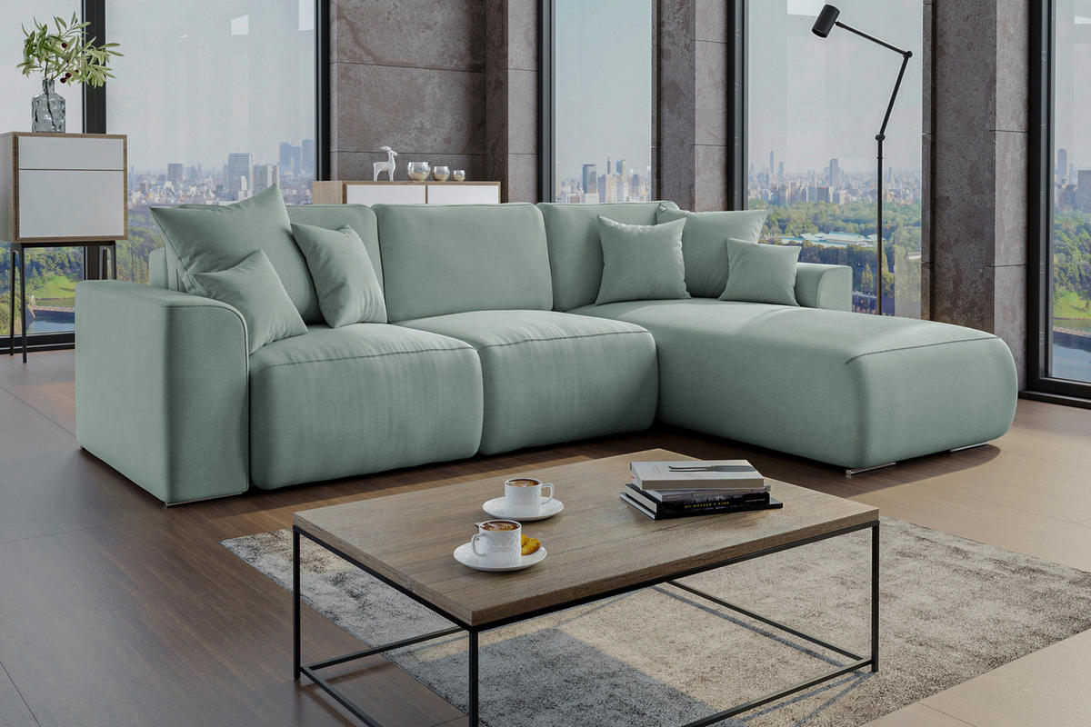 Carryhome ECKSOFA Mintgrün Velours, links davon: Regal, rechts davon: Hochflorteppich, Couchtisch, Lektüre in hellem Wohnzimmer.