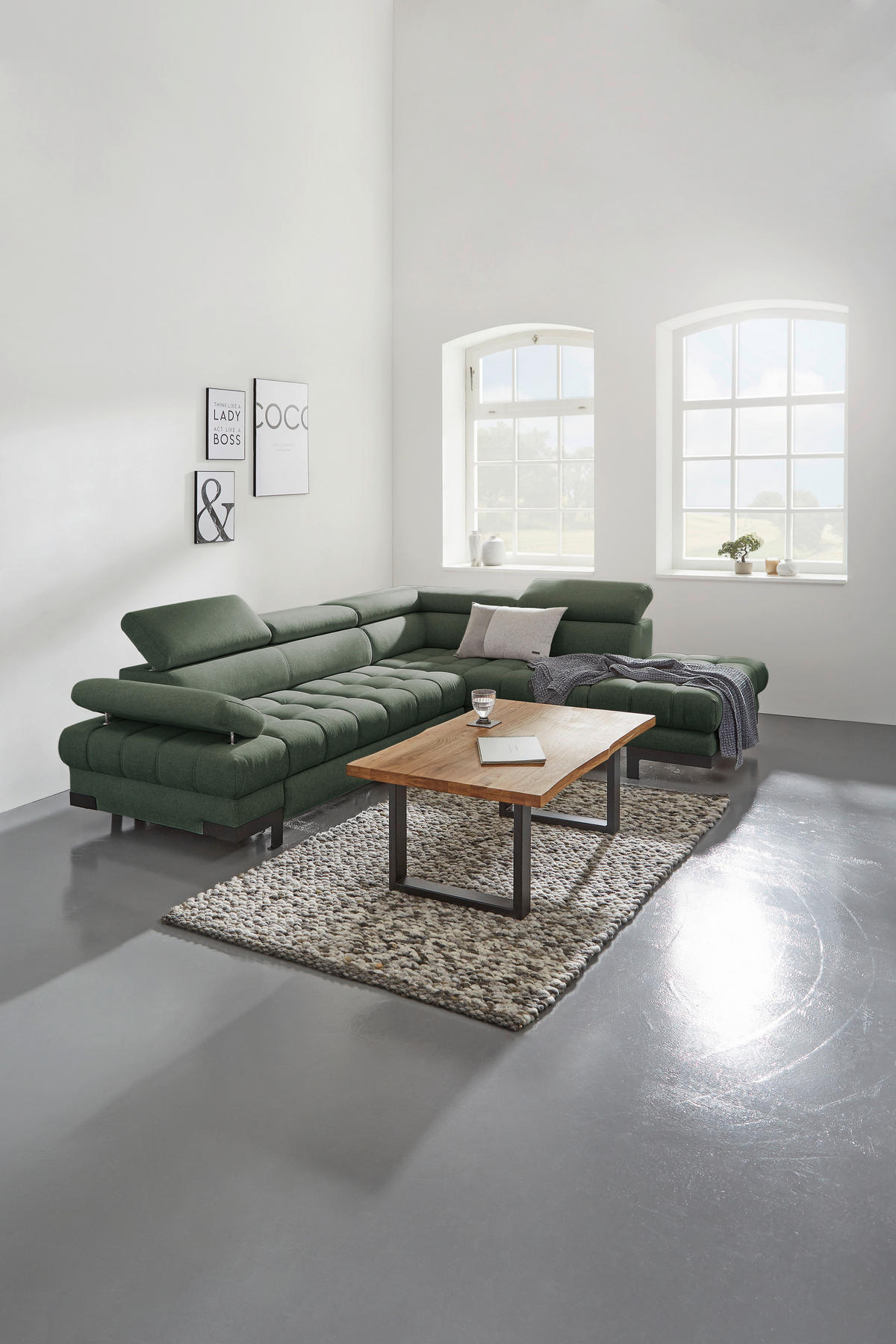 Welnova ECKSOFA Dunkelgrün Webstoff, rechts davon: Hochflorteppich in grau, Couchtisch, Kissen in weiß, Topfpflanze in hellem Wohnzimmer.