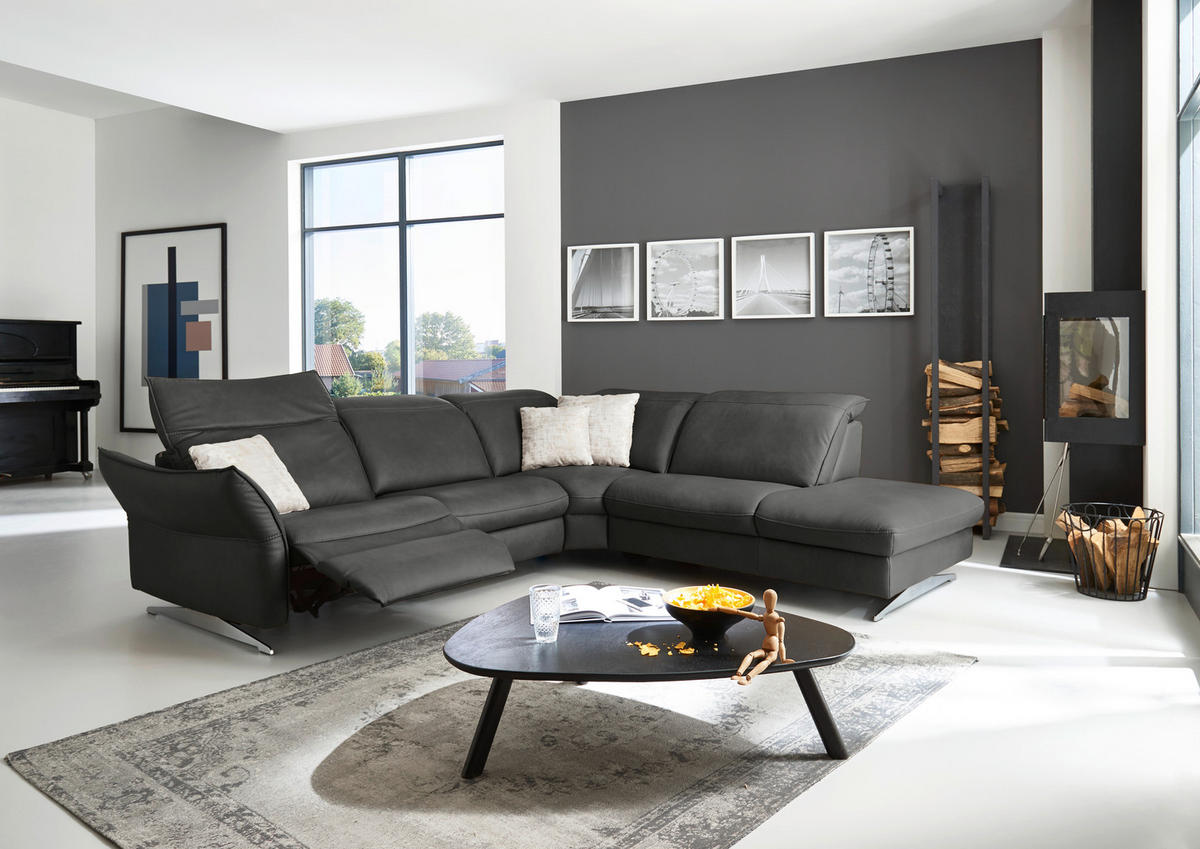 Hukla ECKSOFA inkl. Funktionen Valdera Schwarz Echtleder, links davon: Hochflorteppich, rechts davon: Couchtisch, Kissen in weiß, Kamin in hellem Wohnzimmer.