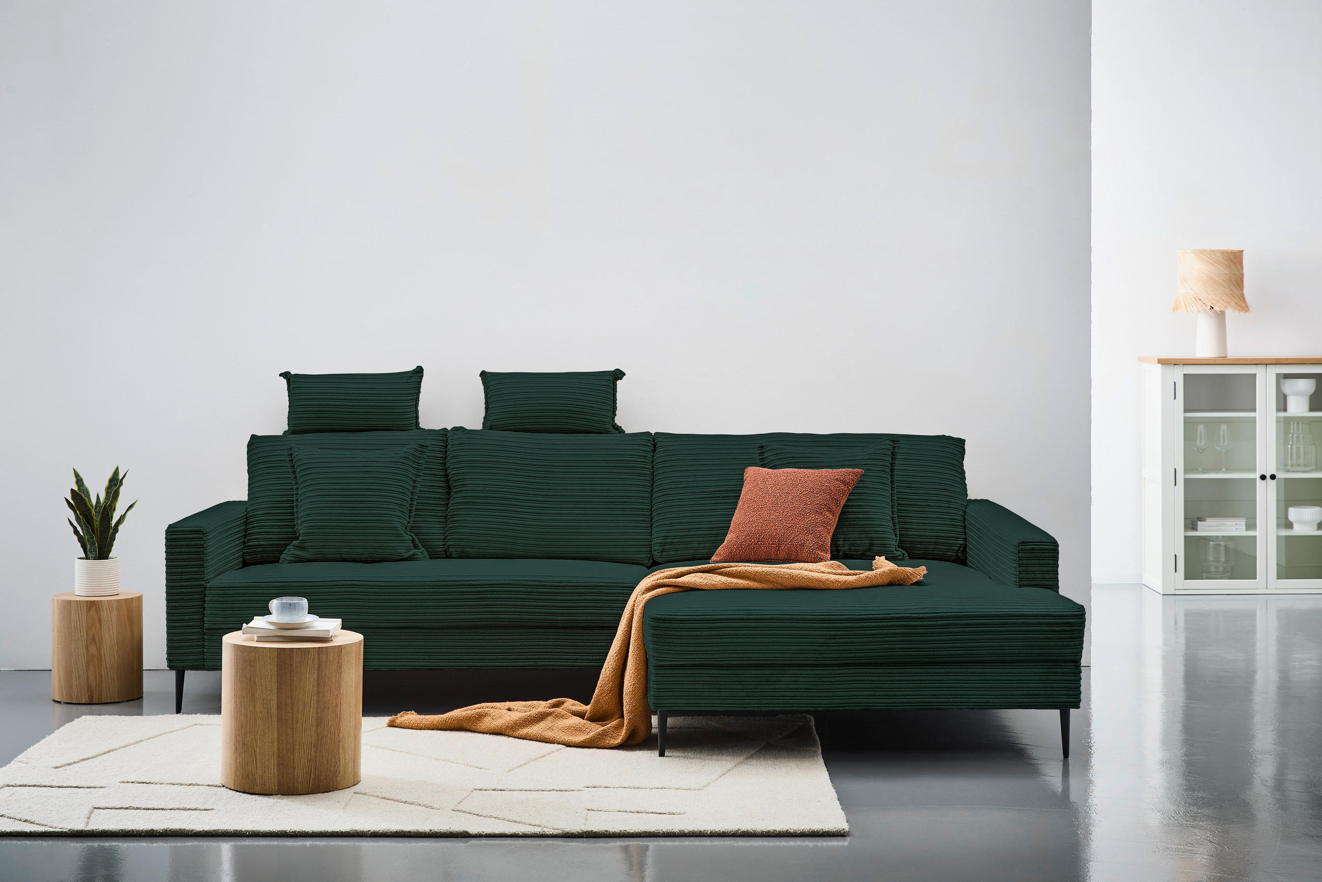 Carryhome ECKSOFA Dunkelgrün Cord, links davon: Sitzbank in grün, Topfpflanze in grün, rechts davon: Regal in hellem Schlafzimmer.