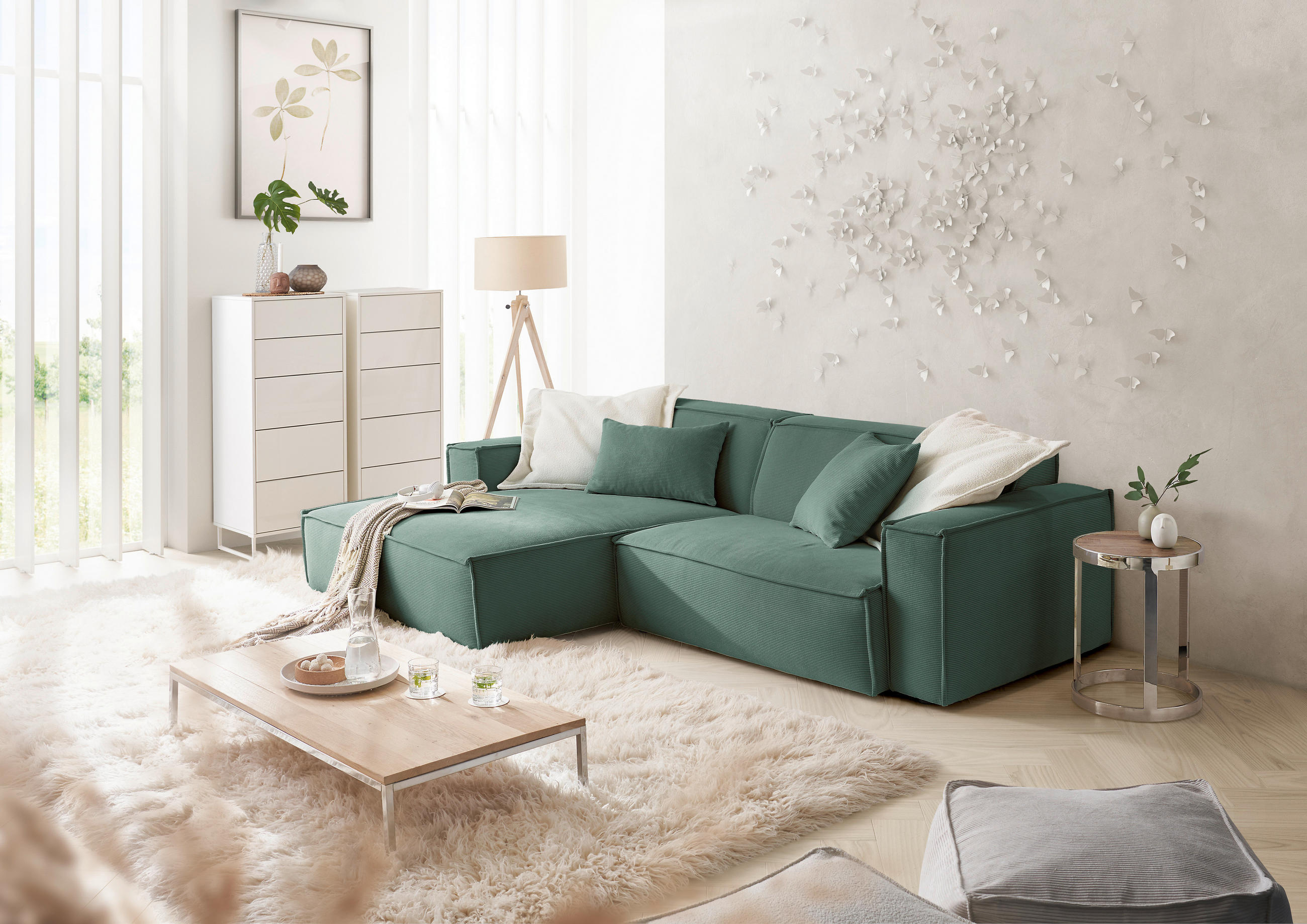 Hom`in ECKSOFA Grün Feincord, links davon: Kunstfell in grün, Couchtisch, Store in weiß, Highboard in hellem Wohnzimmer.