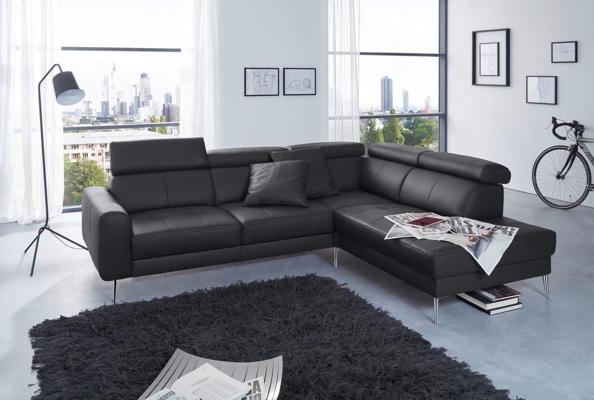 Hom`in ECKSOFA Schwarz Echtleder, links davon: Hochflorteppich in grau, Store in weiß, rechts davon: Kissen, Lektüre in hellem Wohnzimmer.