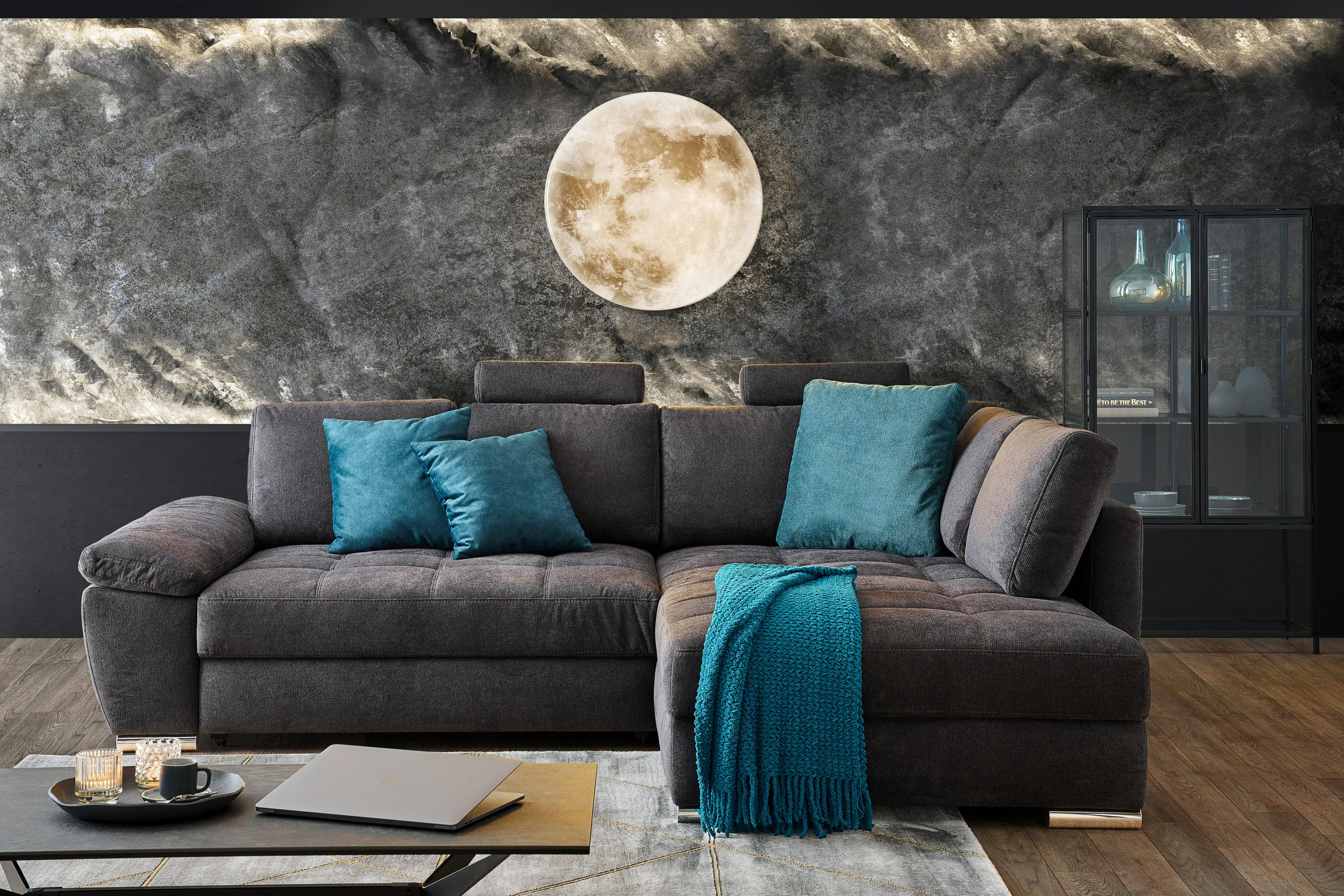 Carryhome ECKSOFA Schwarz, Petrol Webstoff, links davon: Hochflorteppich, rechts davon: Regal, Kissen, Lektüre in dunklem Wohnzimmer.
