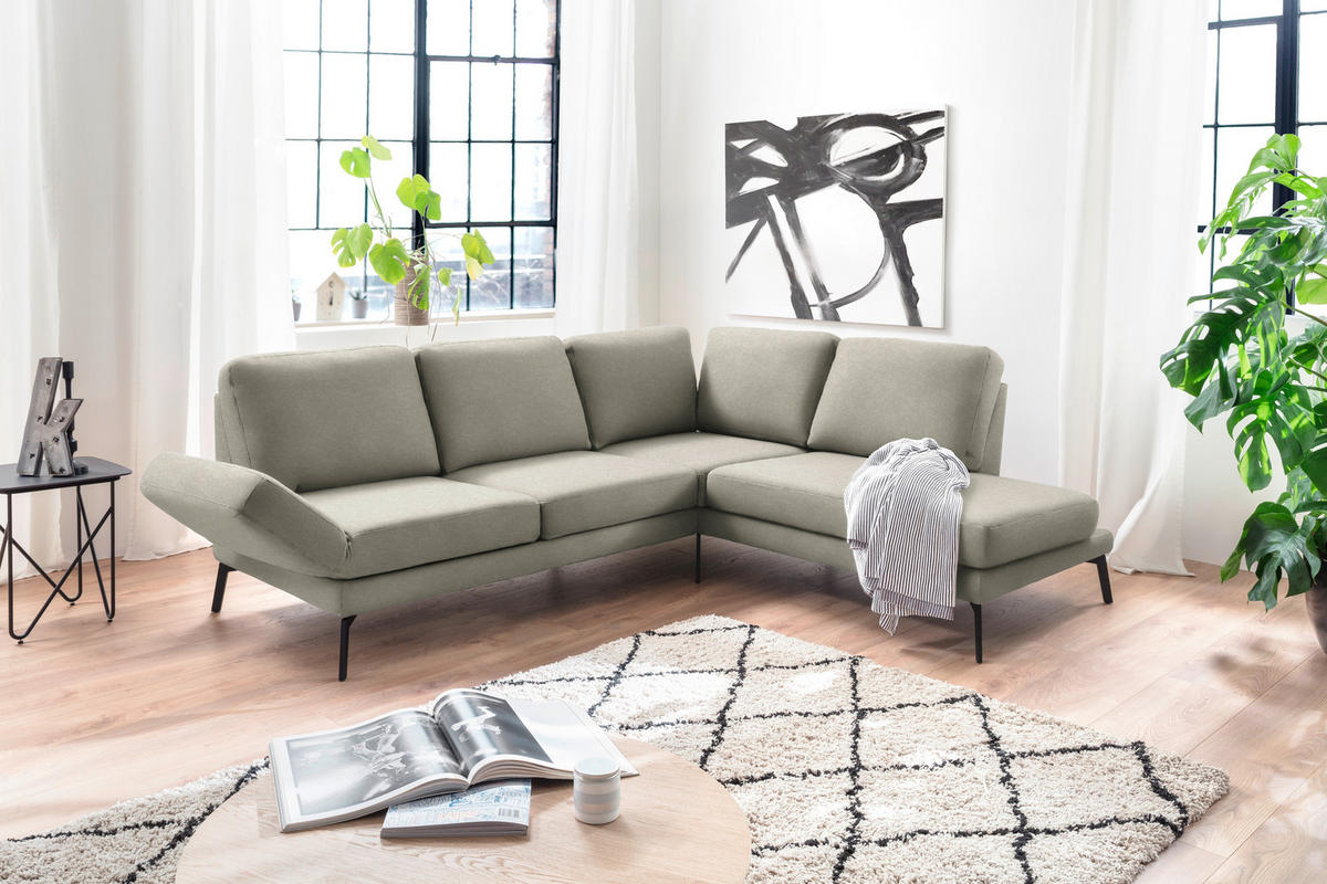 Hom`in ECKSOFA Olivgrün Mikrofaser, links davon: Lektüre, rechts davon: Hochflorteppich in weiß, Bild in schwarz, Topfpflanze in grün in hellem Wohnzimmer.