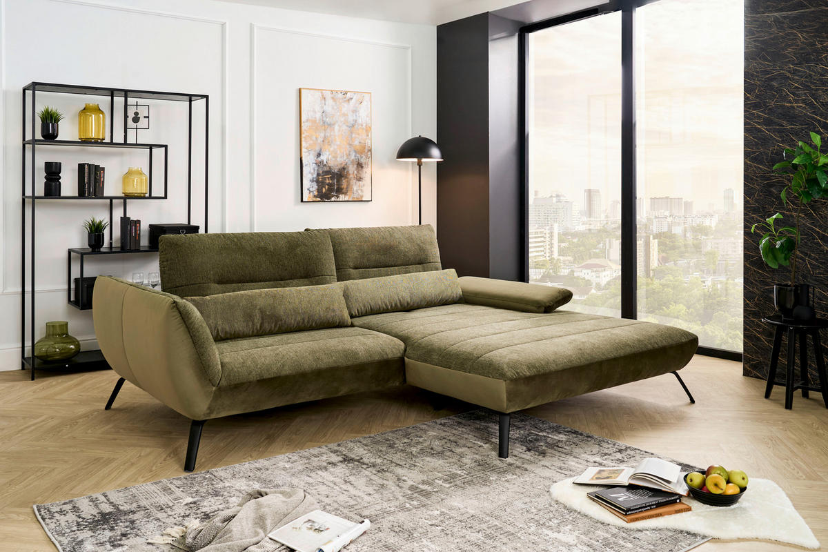 Carryhome ECKSOFA Olivgrün Webstoff, links davon: Webteppich, Regal in grün, rechts davon: Lektüre in schwarz, Bild in hellem Wohnzimmer.