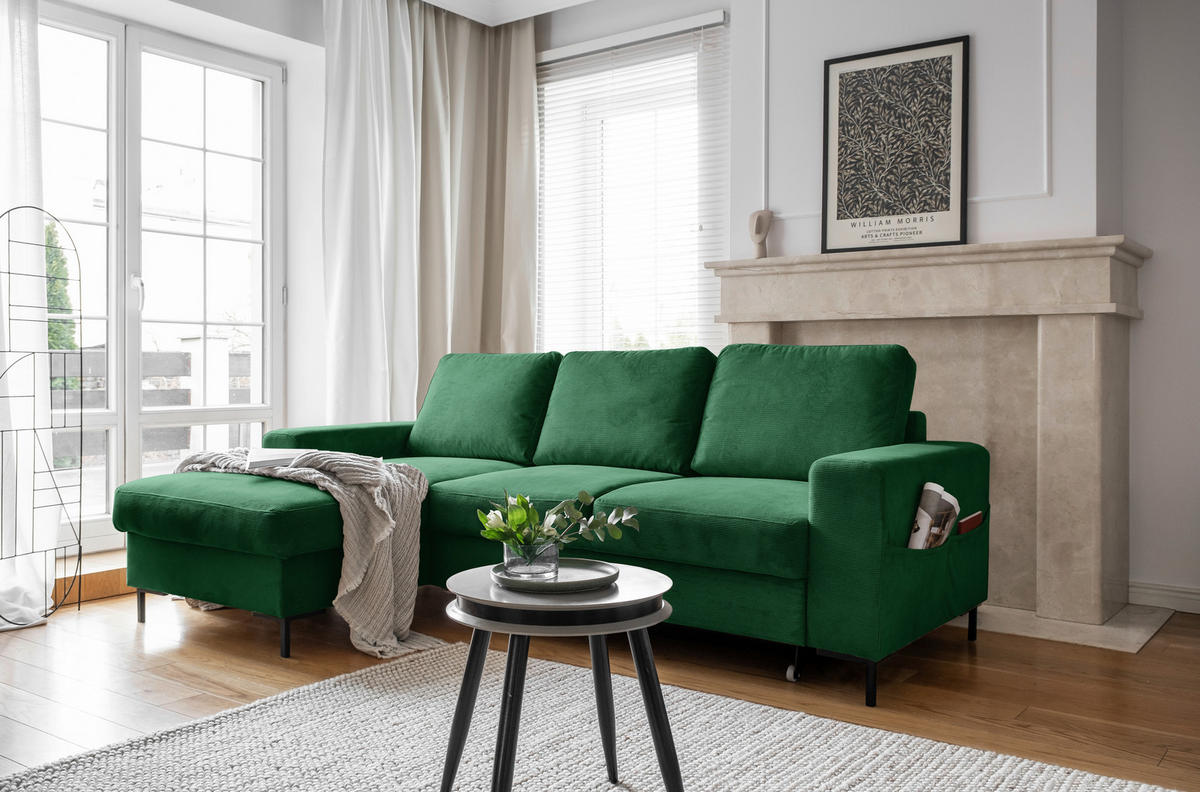 MID.YOU ECKSOFA Smaragdgrün Cord, links davon: Hochflorteppich, Decke in grün, rechts davon: Beistelltisch, Jalousie in weiß in hellem Wohnzimmer.