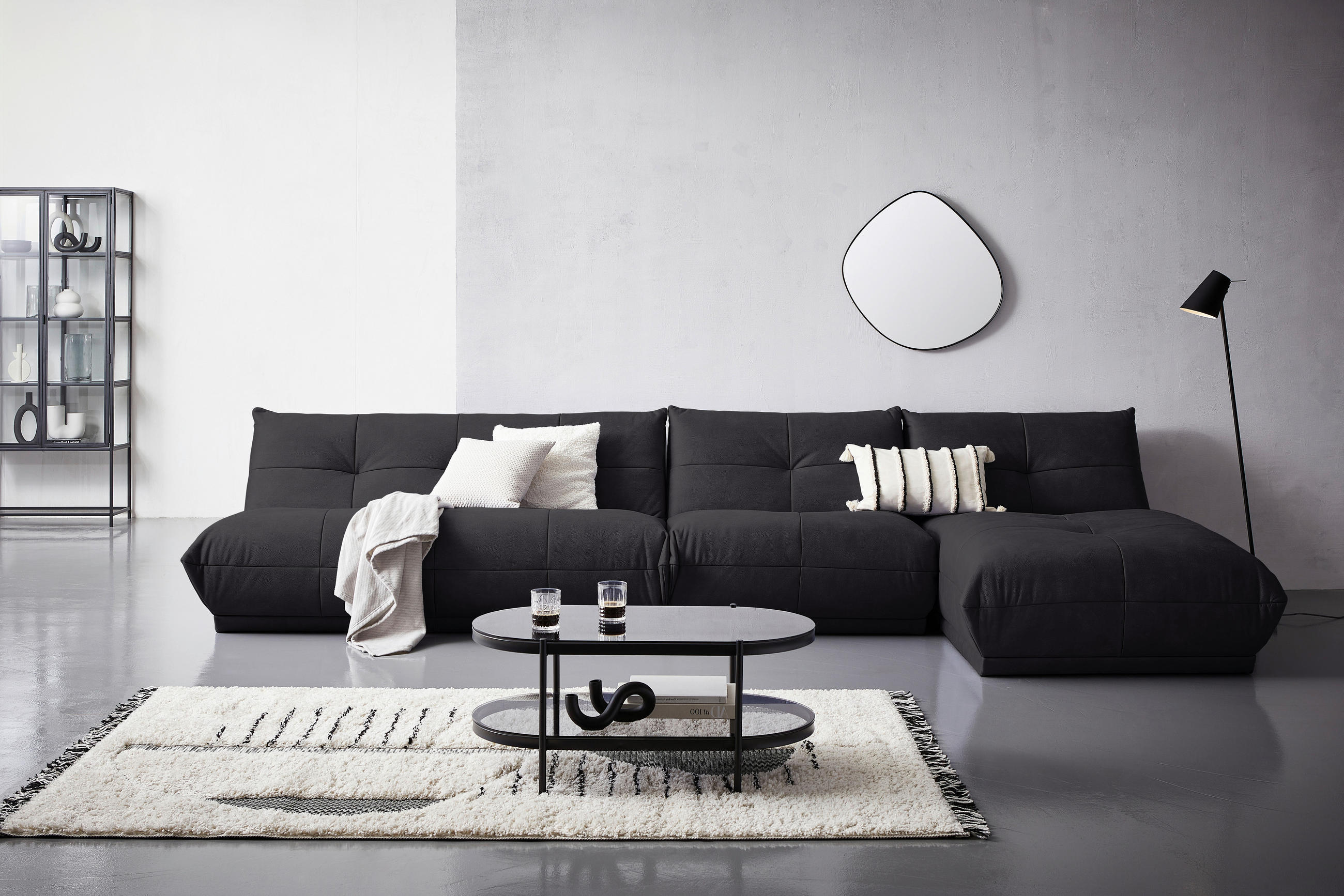 Livetastic ECKSOFA Schwarz Lederlook, links davon: Hochflorteppich, Regal, rechts davon: Couchtisch in schwarz, Spiegel in weiß in hellem Wohnzimmer.
