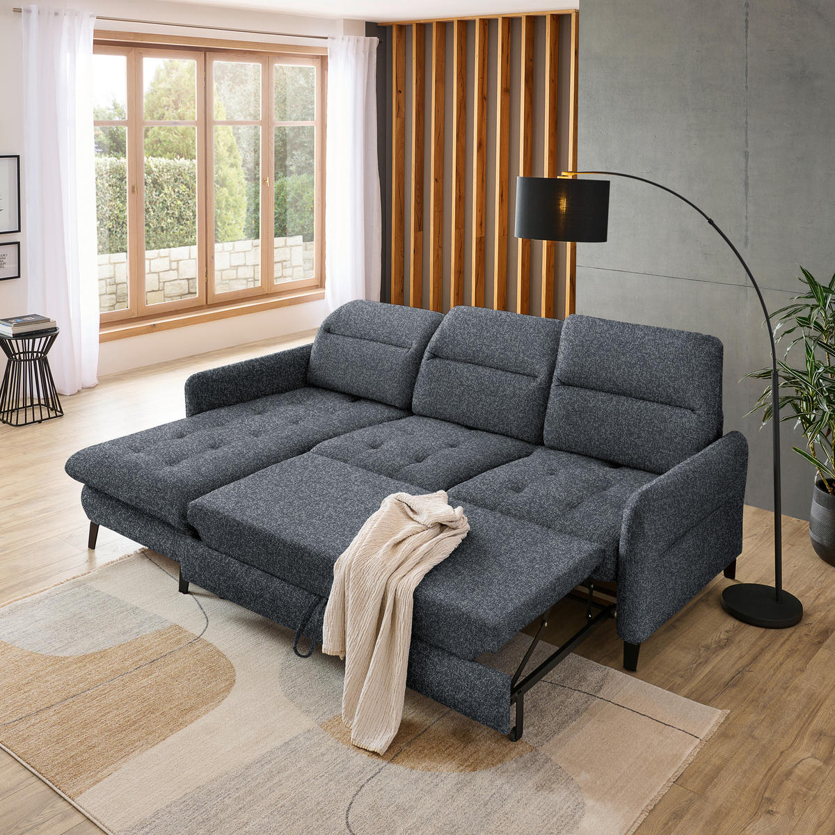 Livetastic ECKSOFA Schwarz Plüsch, links davon: Hochflorteppich in grau, Store in weiß, rechts davon: Gardine, Topfpflanze in grau in hellem Wohnzimmer.