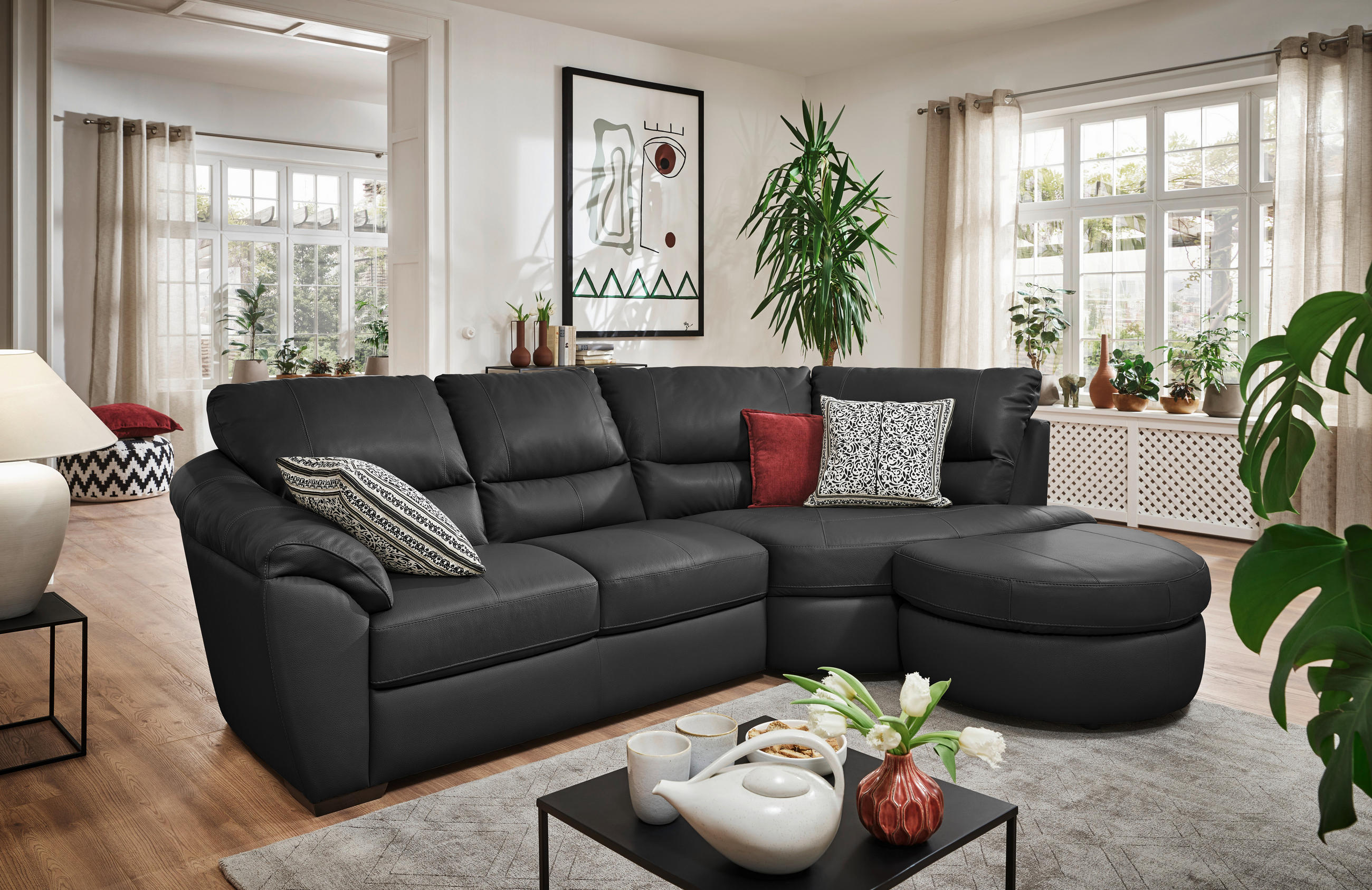 Livetastic ECKSOFA Schwarz Kombination Echtleder/Lederlook, links davon: Kissen, rechts davon: Hochflorteppich, Couchtisch, Bild in hellem Wohnzimmer.