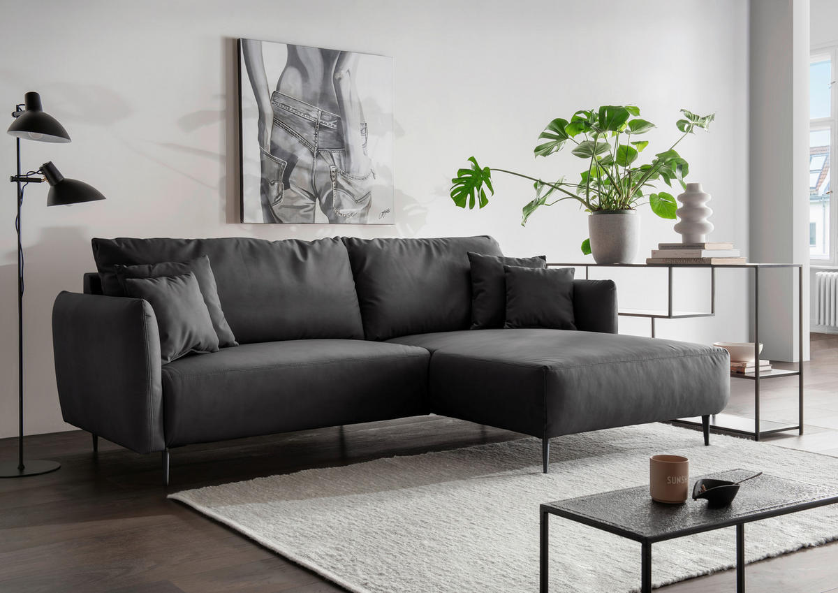 Livetastic ECKSOFA Schwarz Lederlook, links davon: Bild in grau, rechts davon: Hochflorteppich, Couchtisch, Topfpflanze in grün in hellem Wohnzimmer.