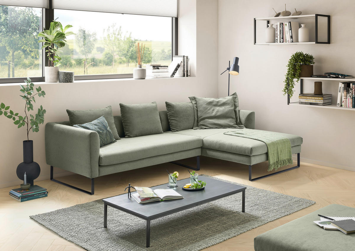Hom`in ECKSOFA Olivgrün Feincord, links davon: Hochflorteppich, Jalousie, rechts davon: Couchtisch, Sitzbank in grün in hellem Wohnzimmer.