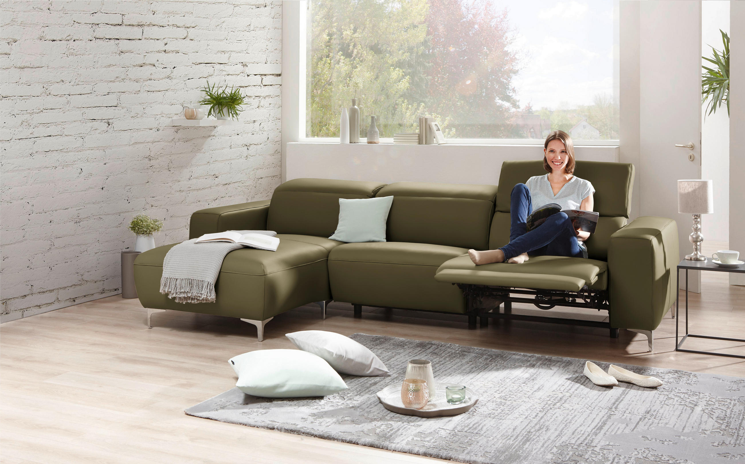 Pure Home Lifestyle ECKSOFA Olivgrün Echtleder, links davon: Kissen in weiß, Decke, rechts davon: Hochflorteppich in weiß, Beistelltisch in hellem Wohnzimmer.