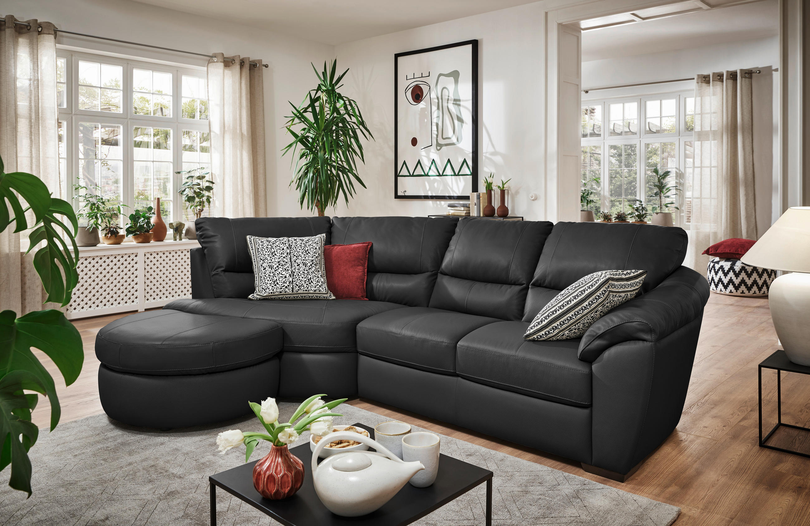 Livetastic ECKSOFA Schwarz Kombination Echtleder/Lederlook, links davon: Hochflorteppich, Sideboard, rechts davon: Couchtisch, Topfpflanze in grün in hellem Wohnzimmer.