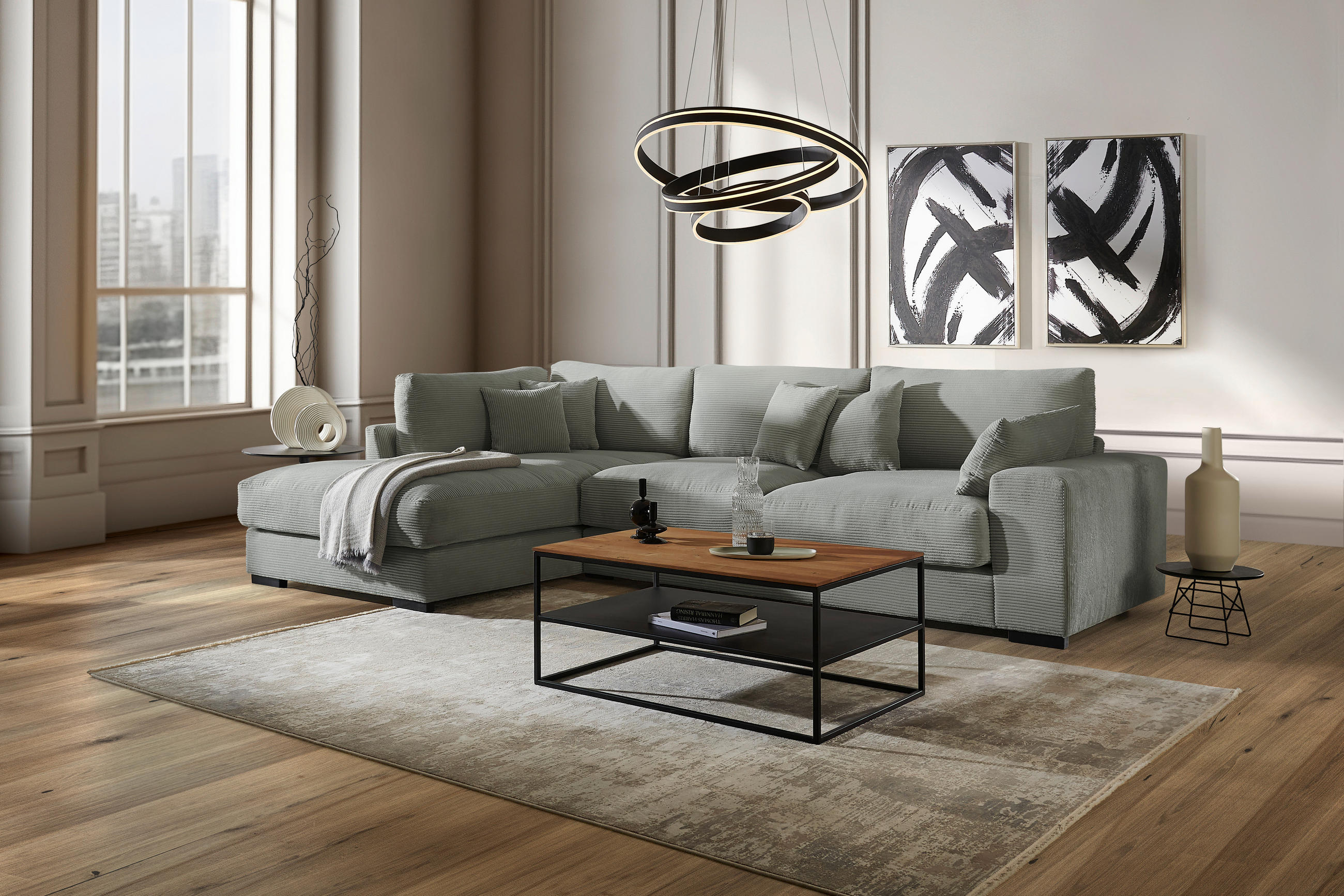 Lomoco ECKSOFA Salbeigrün Cord, links davon: Hochflorteppich, rechts davon: Couchtisch in schwarz, Bild in schwarz, Beistelltisch in hellem Wohnzimmer.