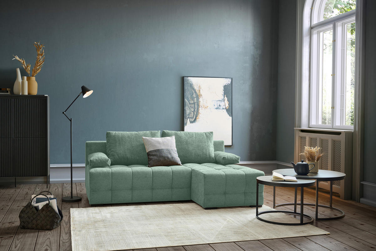 home24 ECKSOFA Dunkelgrün Chenille, rechts davon: Hochflorteppich, Couchtisch, Regal, Bild in dunklem Wohnzimmer.