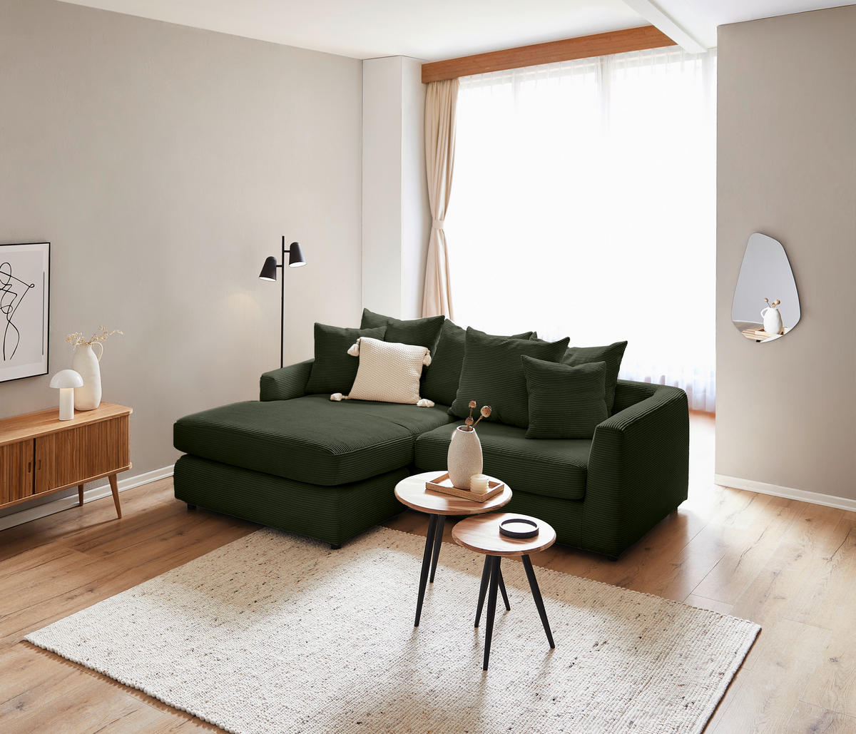 home24 ECKSOFA Dunkelgrün Cord, links davon: Hochflorteppich in weiß, Sofa in grün, rechts davon: Beistelltisch, Wandleuchte in weiß in hellem Wohnzimmer.