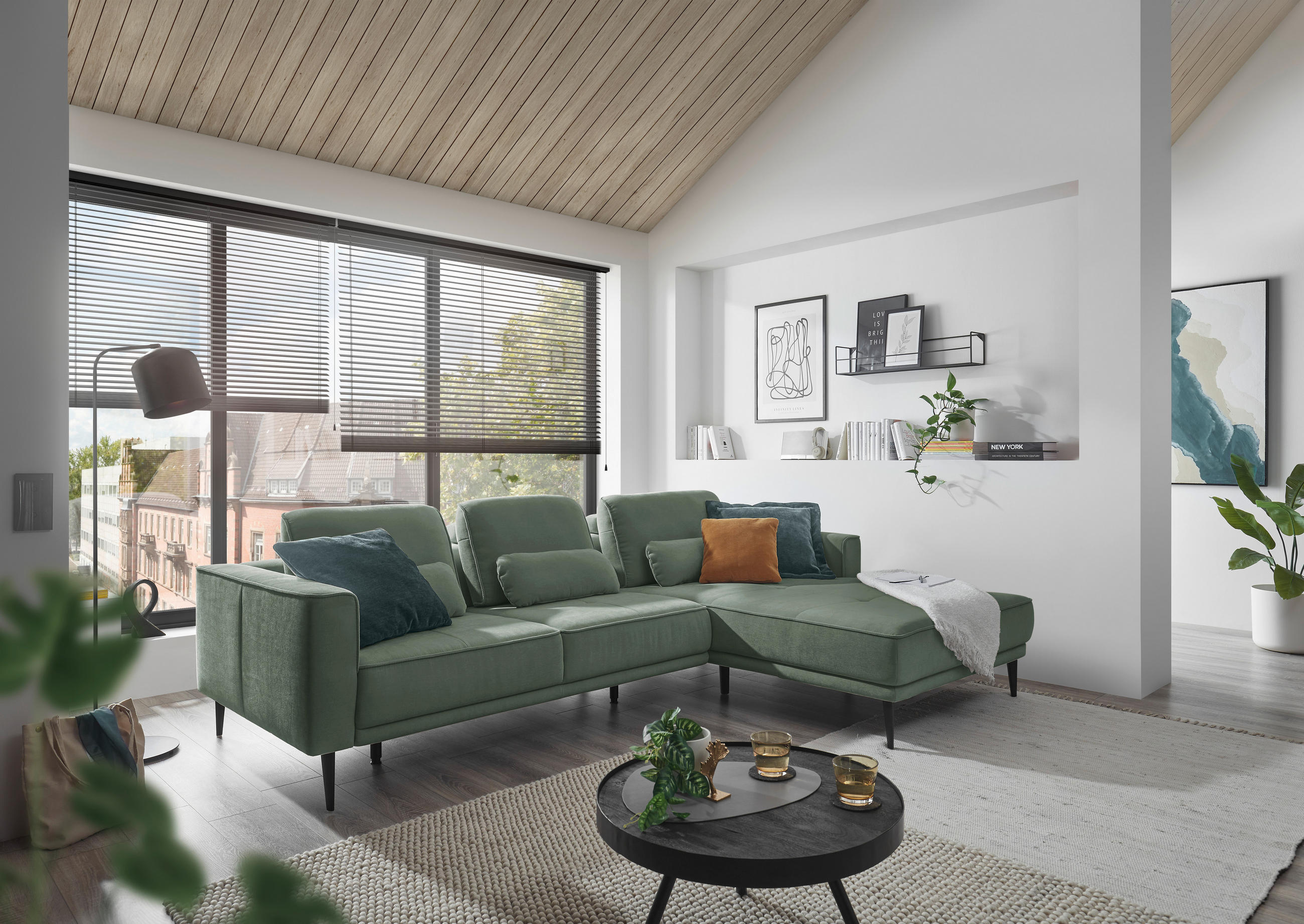 SetOne by Musterring ECKSOFA Dunkelgrün Flachgewebe, links davon: Kissen, rechts davon: Webteppich, Couchtisch, Decke in grün in hellem Wohnzimmer.