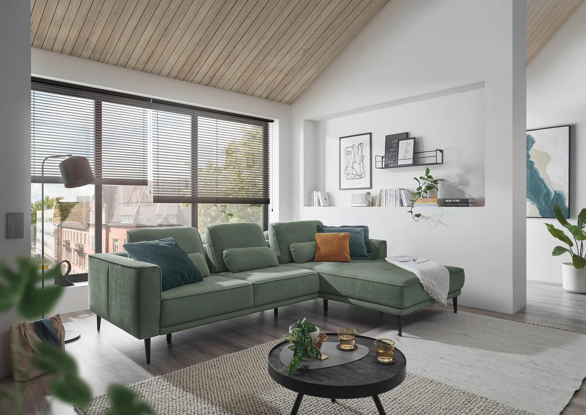 SetOne by Musterring ECKSOFA Dunkelgrün Flachgewebe, links davon: Kissen, rechts davon: Webteppich, Couchtisch, Decke in grün in hellem Wohnzimmer.