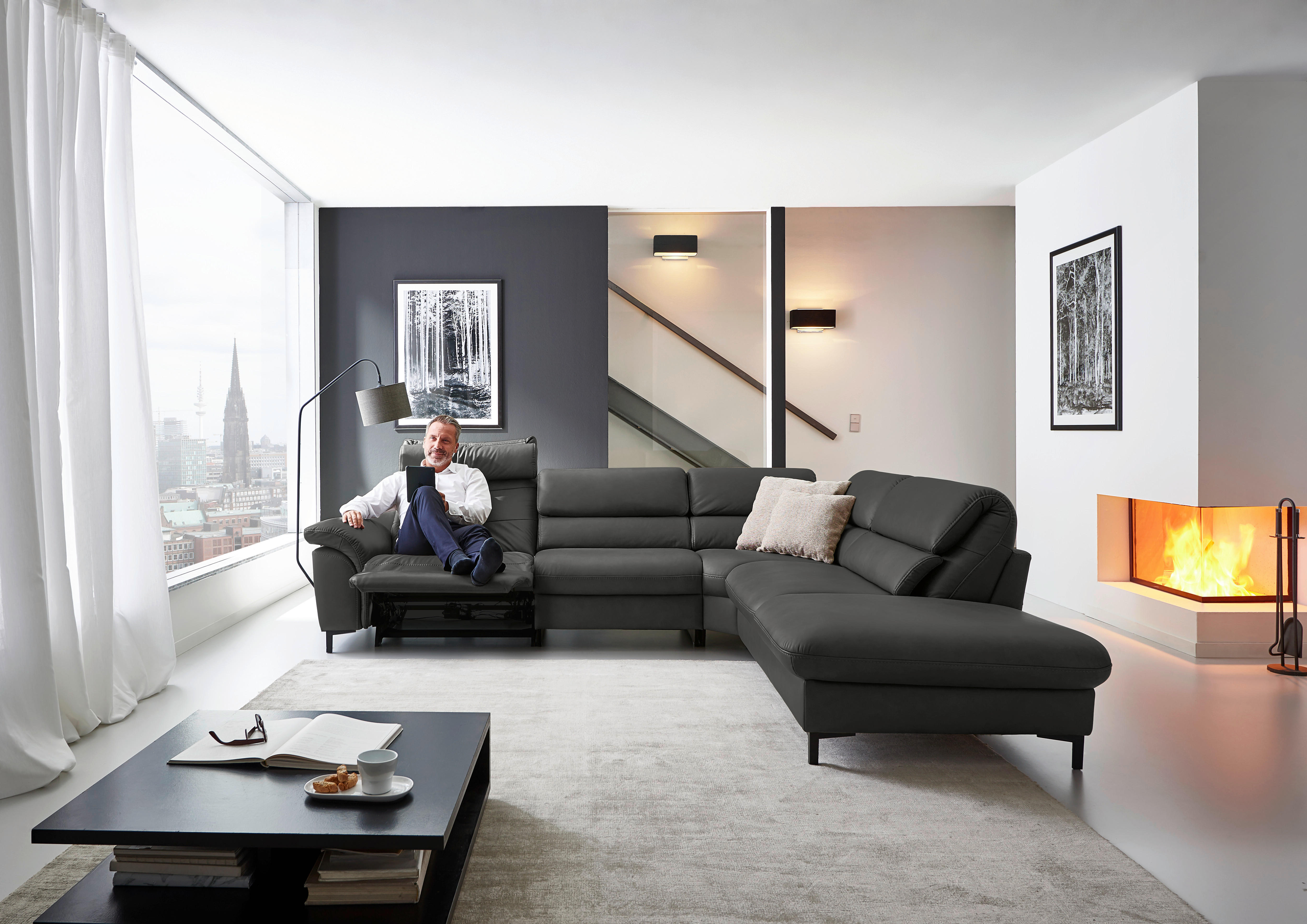 Hukla ECKSOFA Valdera Schwarz Echtleder, links davon: Couchtisch in schwarz, Store in weiß, Lektüre, rechts davon: Kissen in weiß in hellem Wohnzimmer.