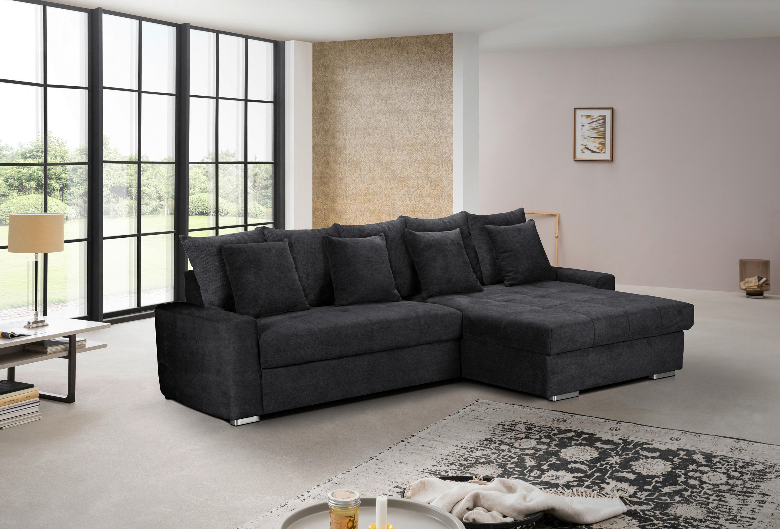 MID.YOU ECKSOFA SALVADOR Schwarz Mikrofaser, links davon: Beistelltisch, Tischleuchte, rechts davon: Hochflorteppich in weiß, Kissen in grau in hellem Wohnzimmer.