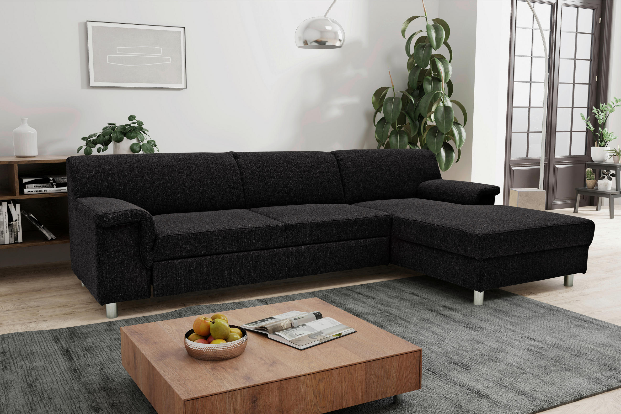MID.YOU ECKSOFA Schwarz Webstoff, links davon: Couchtisch, Bild in weiß, rechts davon: Lektüre in weiß, Topfpflanze in grün in hellem Wohnzimmer.