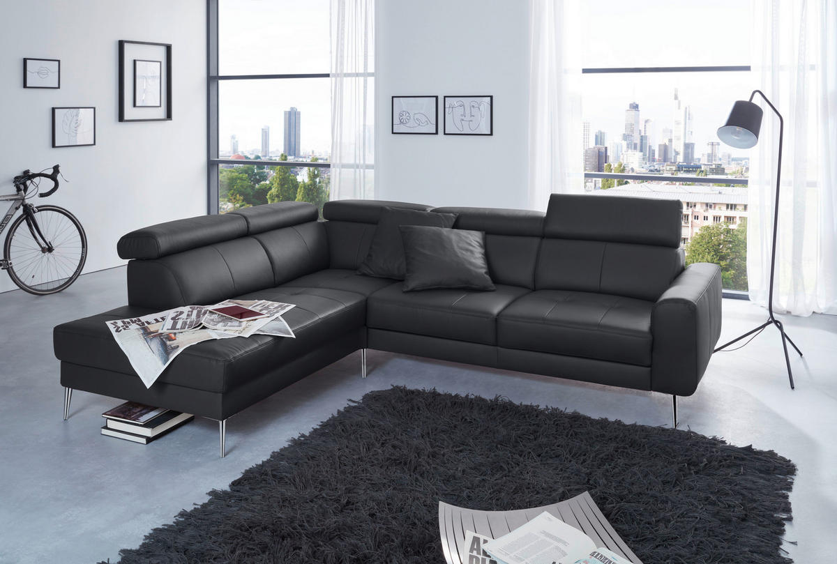 Hom`in ECKSOFA Schwarz Echtleder, links davon: Lektüre, rechts davon: Hochflorteppich, Kissen, Store in weiß in hellem Wohnzimmer.