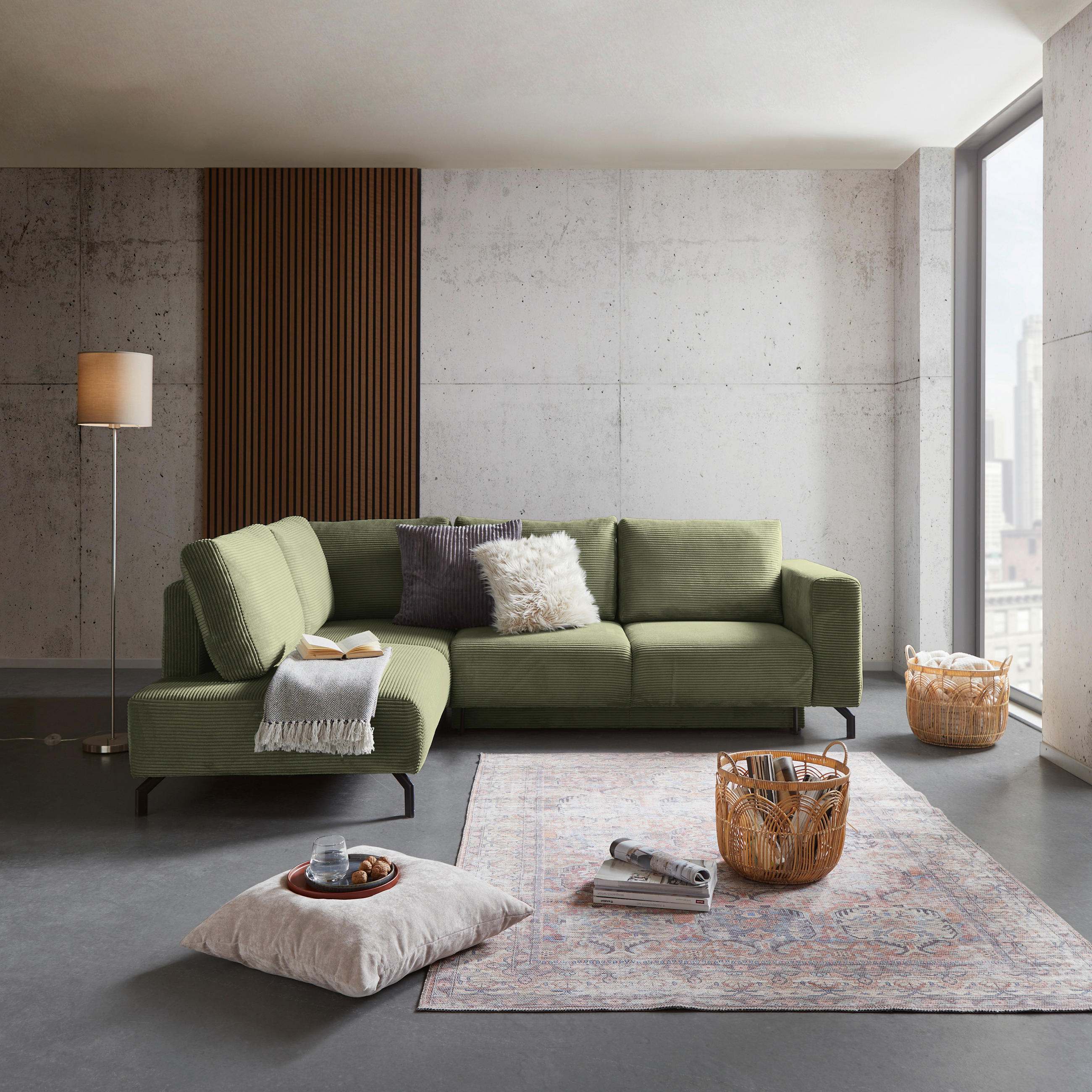 P & B ECKSOFA Grün Cord, links davon: Lektüre, Stehleuchte, rechts davon: Hochflorteppich, Kissen in weiß in hellem Wohnzimmer.