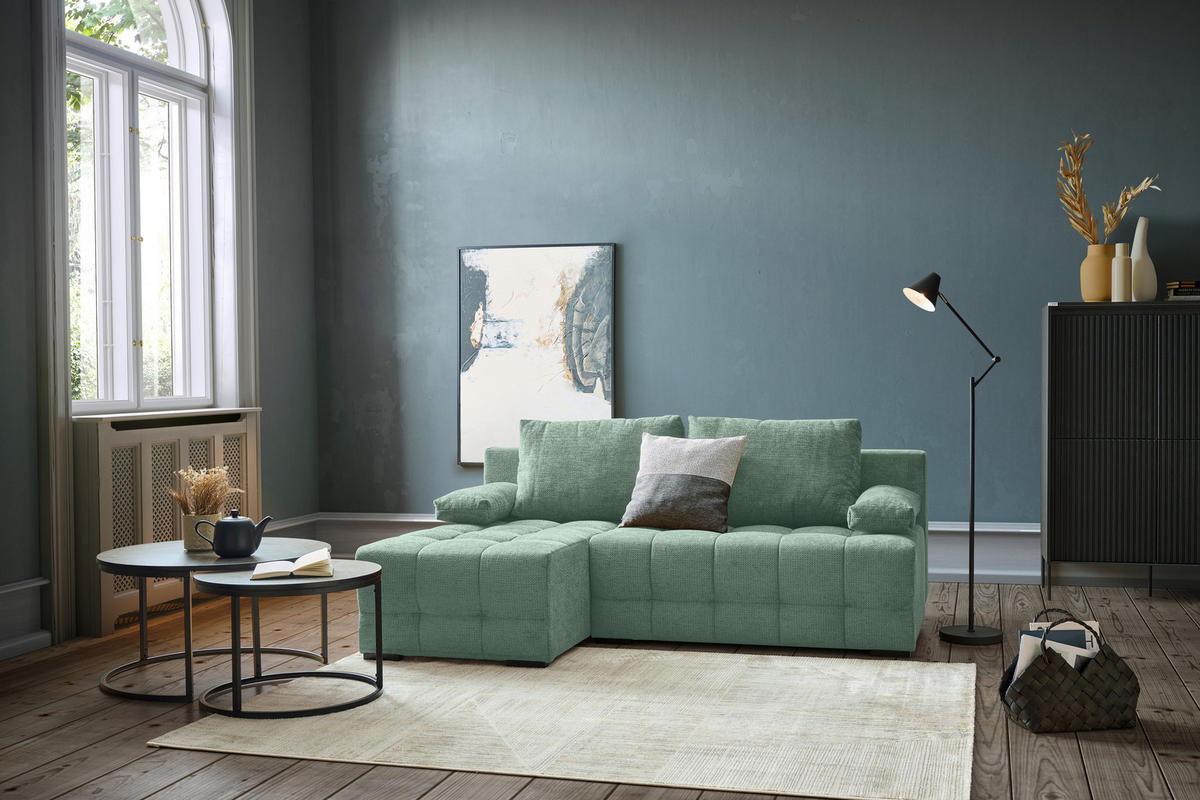 home24 ECKSOFA Dunkelgrün Chenille, links davon: Hochflorteppich in grün, Couchtisch, Bild, rechts davon: Highboard in dunklem Wohnzimmer.