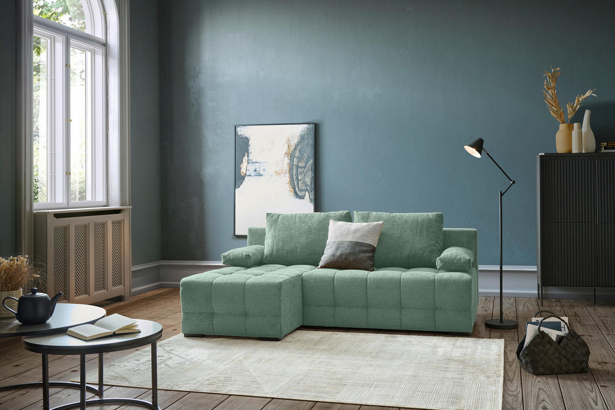 home24 ECKSOFA Dunkelgrün Chenille, links davon: Hochflorteppich, Beistelltisch, Bild in blau, rechts davon: Stehleuchte in grün in dunklem Wohnzimmer.
