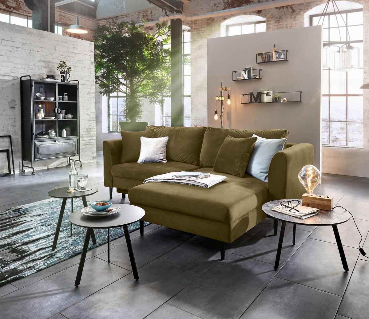 Ti'me ECKSOFA Grün Velours, links davon: Lektüre in weiß, Vitrine in schwarz, Kissen in weiß, rechts davon: Beistelltisch in hellem Wohnzimmer.