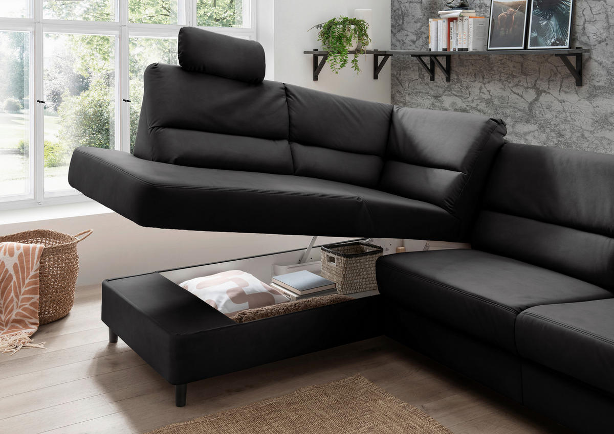 Livetastic ECKSOFA Schwarz Lederlook, links davon: Hochflorteppich, Kissen in weiß, Hocker, rechts davon: Topfpflanze in grün in dunklem Wohnzimmer.