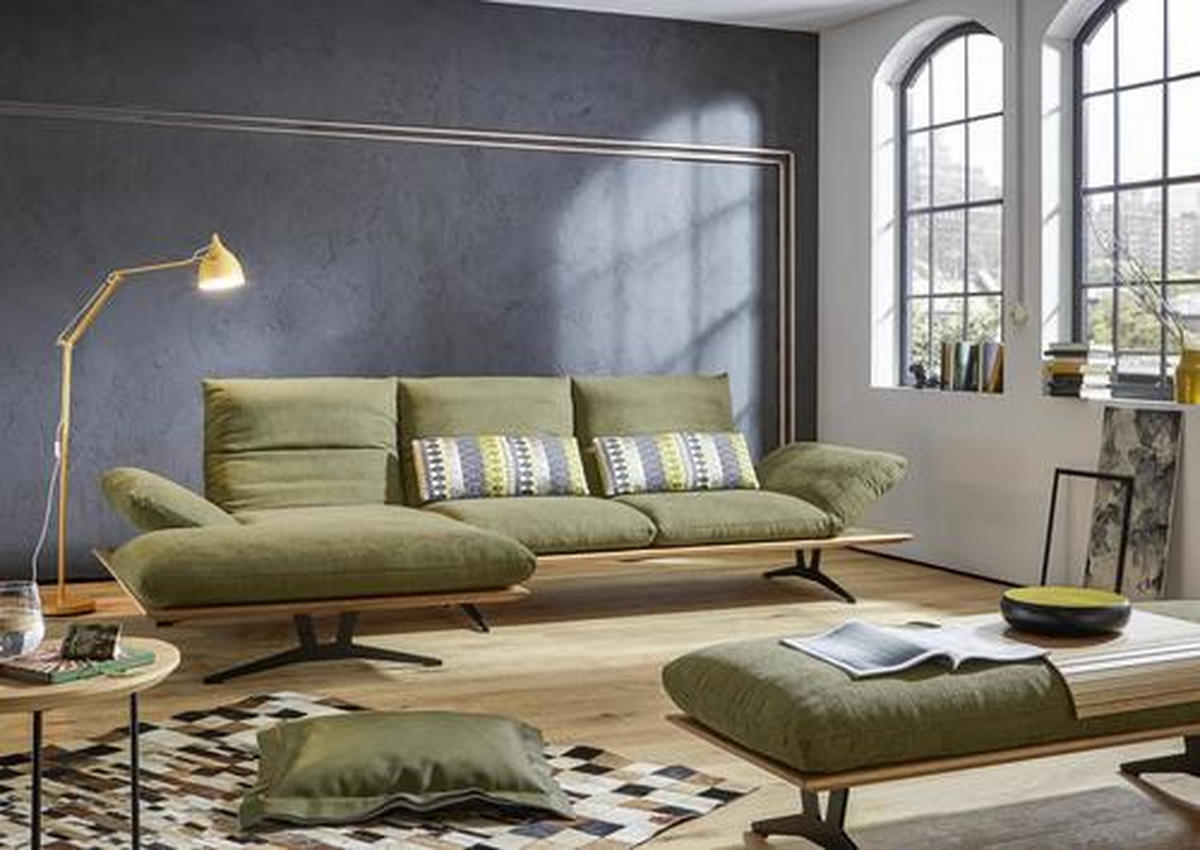 Dieter Knoll ECKSOFA Grün Flachgewebe, links davon: Kunstfell in grün, Beistelltisch, rechts davon: Lektüre in weiß, Kissen in hellem Wohnzimmer.
