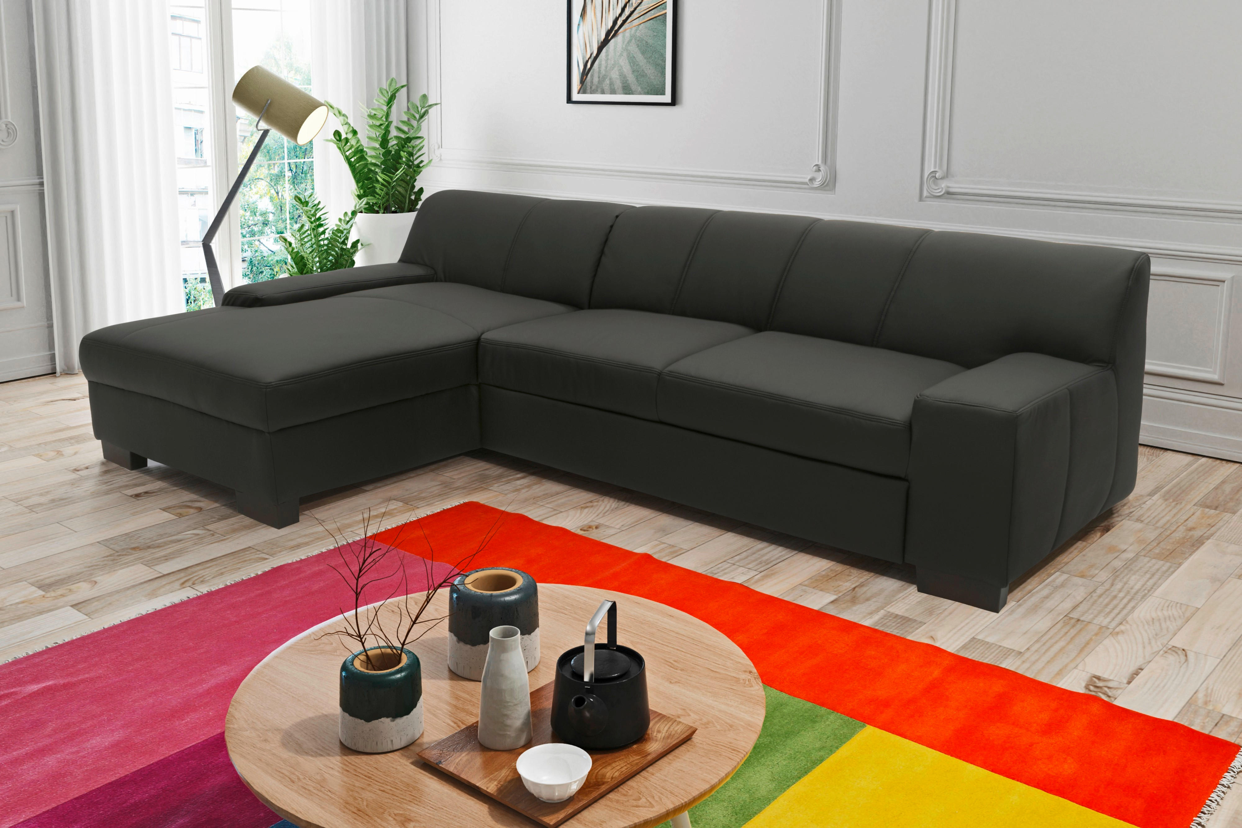 MID.YOU ECKSOFA Schwarz Lederlook, links davon: Hochflorteppich, Gardine, Topfpflanze in grün, rechts davon: Bild in hellem Wohnzimmer.