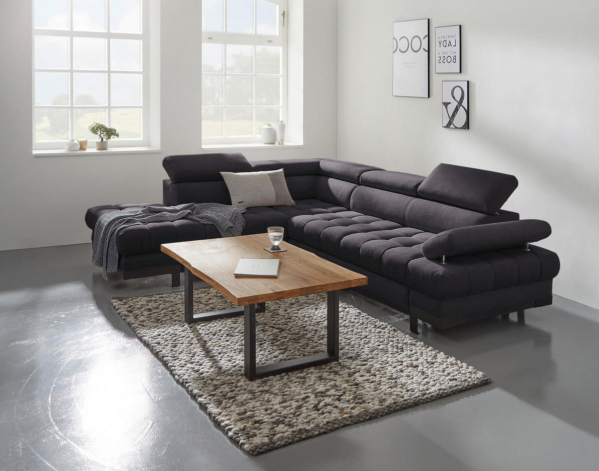 Welnova ECKSOFA Schwarz Webstoff, links davon: Hochflorteppich in grau, Couchtisch, rechts davon: Kissen, Bild in hellem Wohnzimmer.